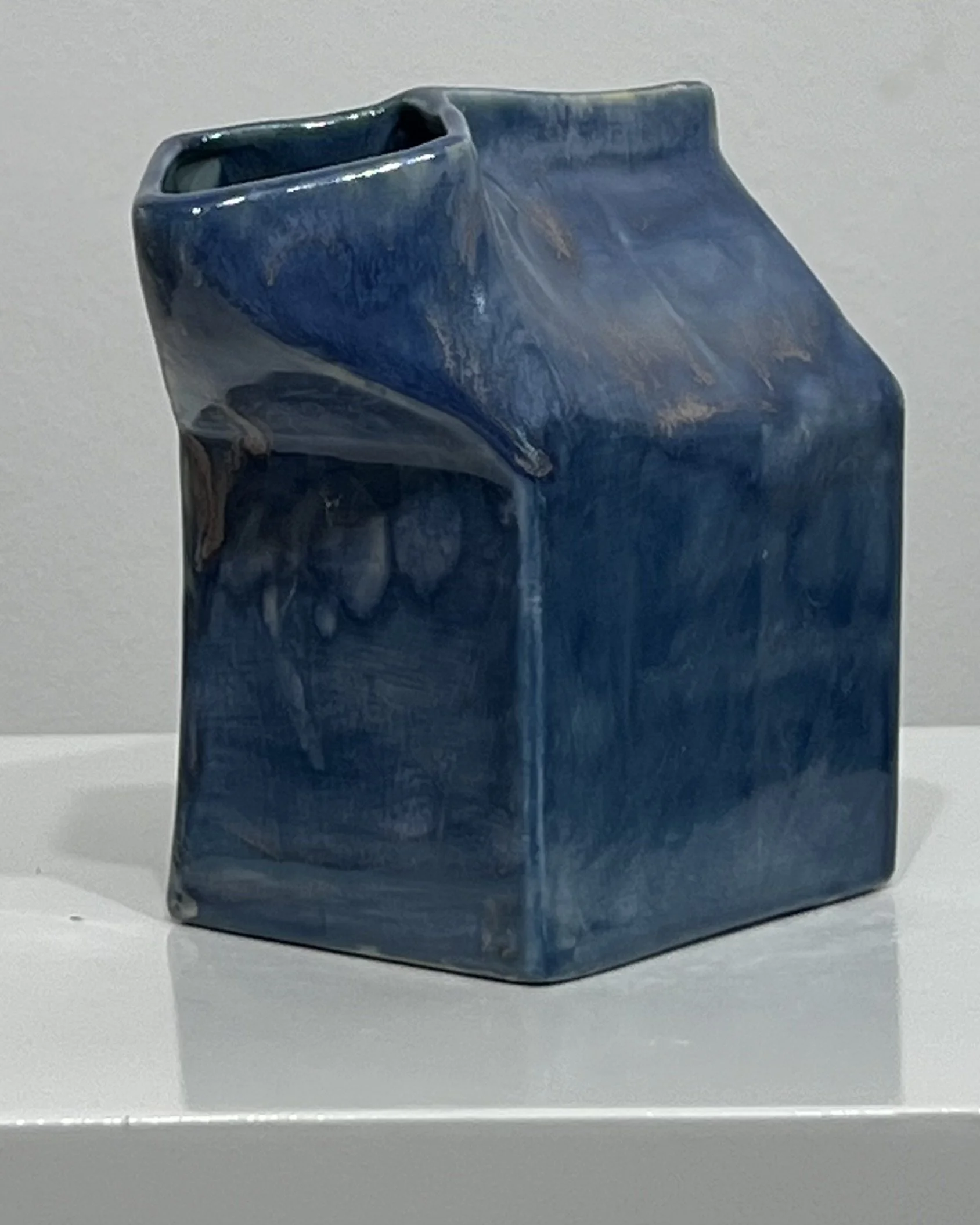 Three-quarter view of Blue Splatter porcelain milk carton sculpture highlighting its geometric form and glossy blue glaze.