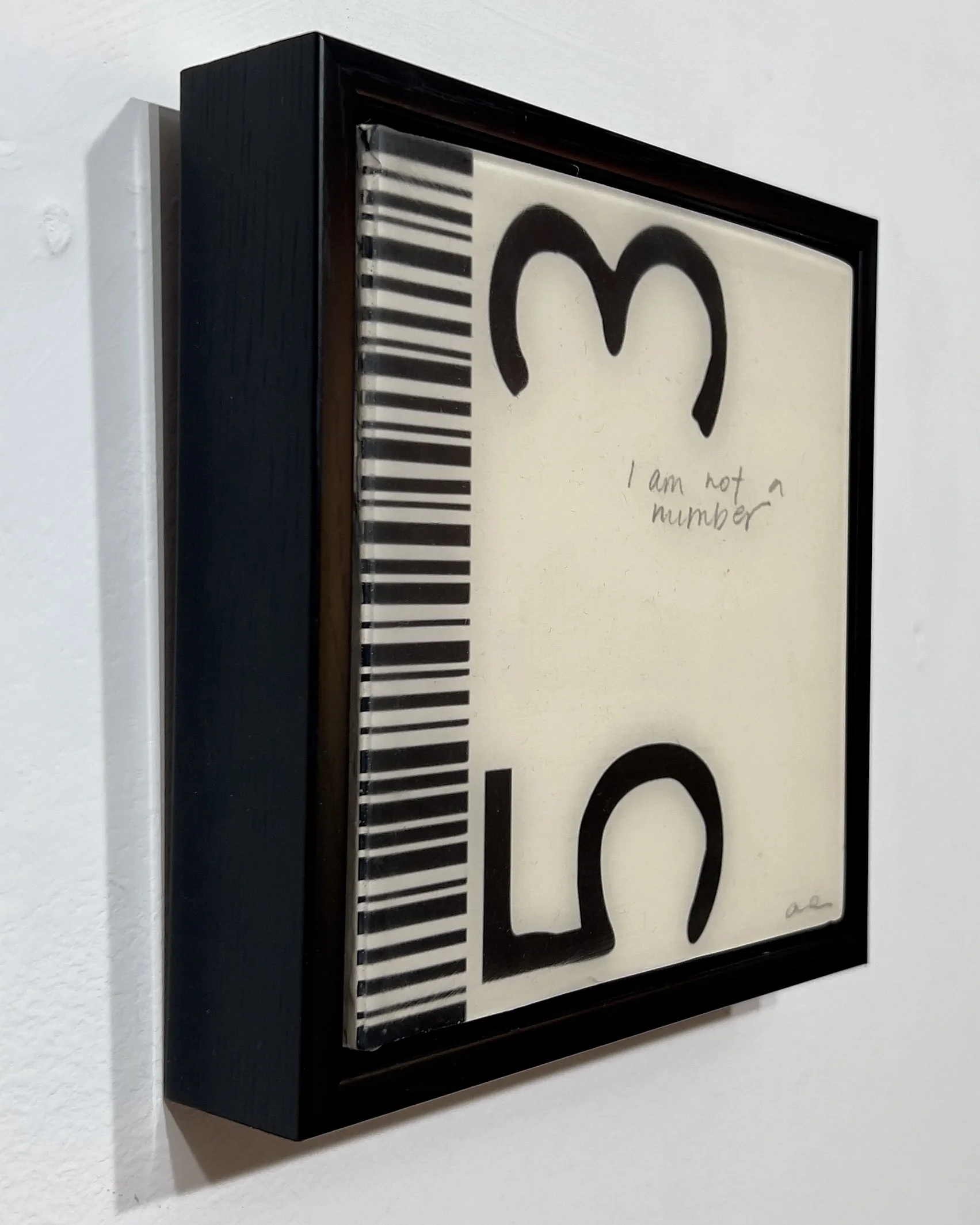 Angled view of I Am Not a Number, an original 6 by 6 inch collage, acrylic and resin artwork on wood in a black frame by Alissa Van Atta.