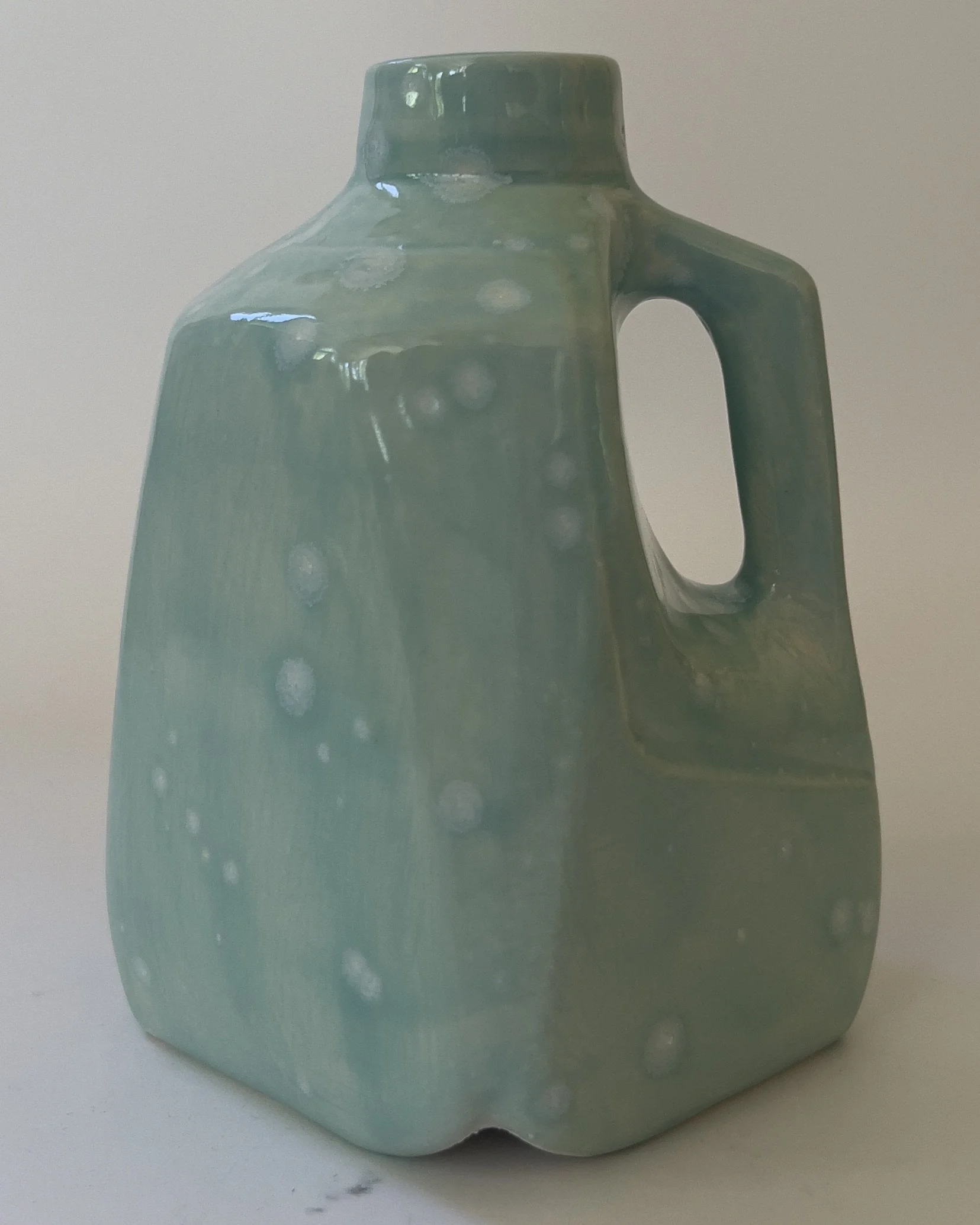 Handmade ceramic milk jug sculpture with celadon bloom glaze viewed from front angle