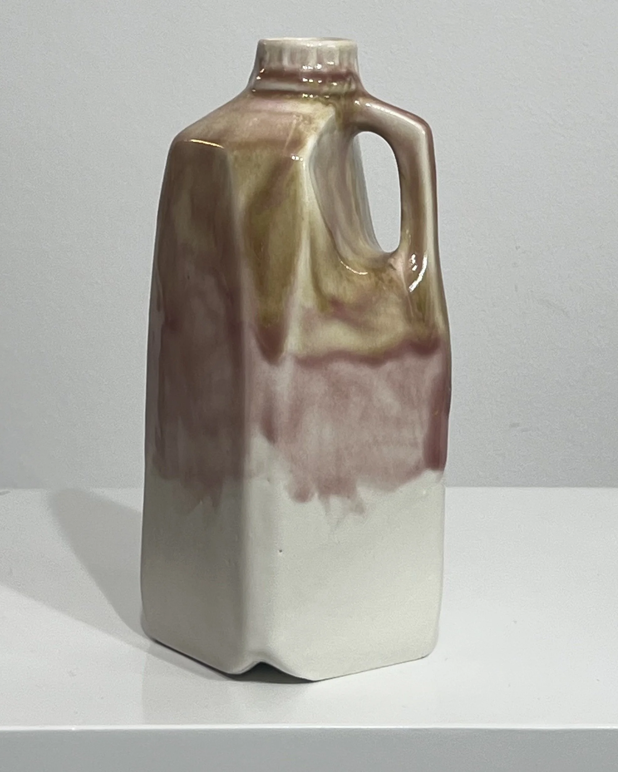 Side view of tall ceramic milk jug showing the sculpted handle and layered olive, pink, plum, and white glaze.