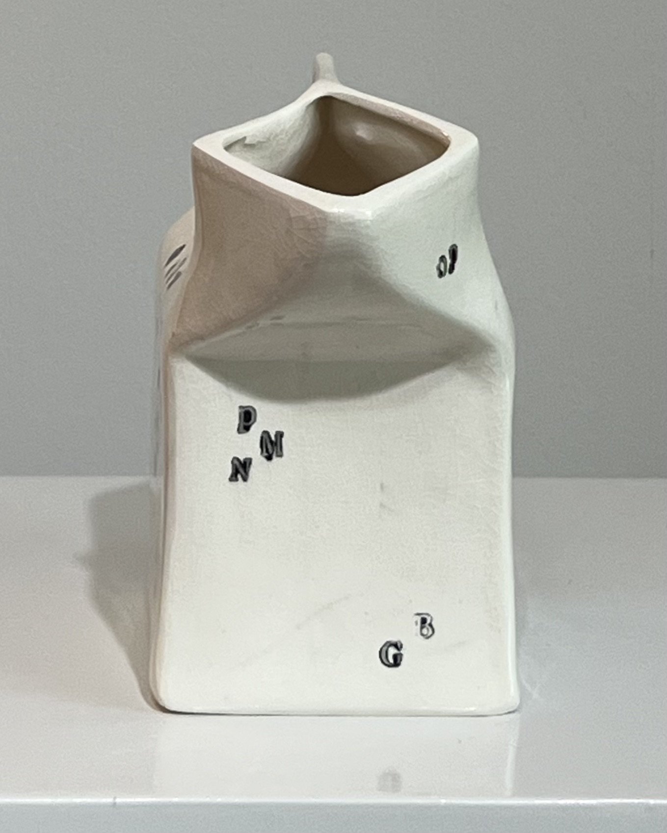 Opposite side view of a handbuilt porcelain milk carton highlighting its folded geometry and typographic surface.