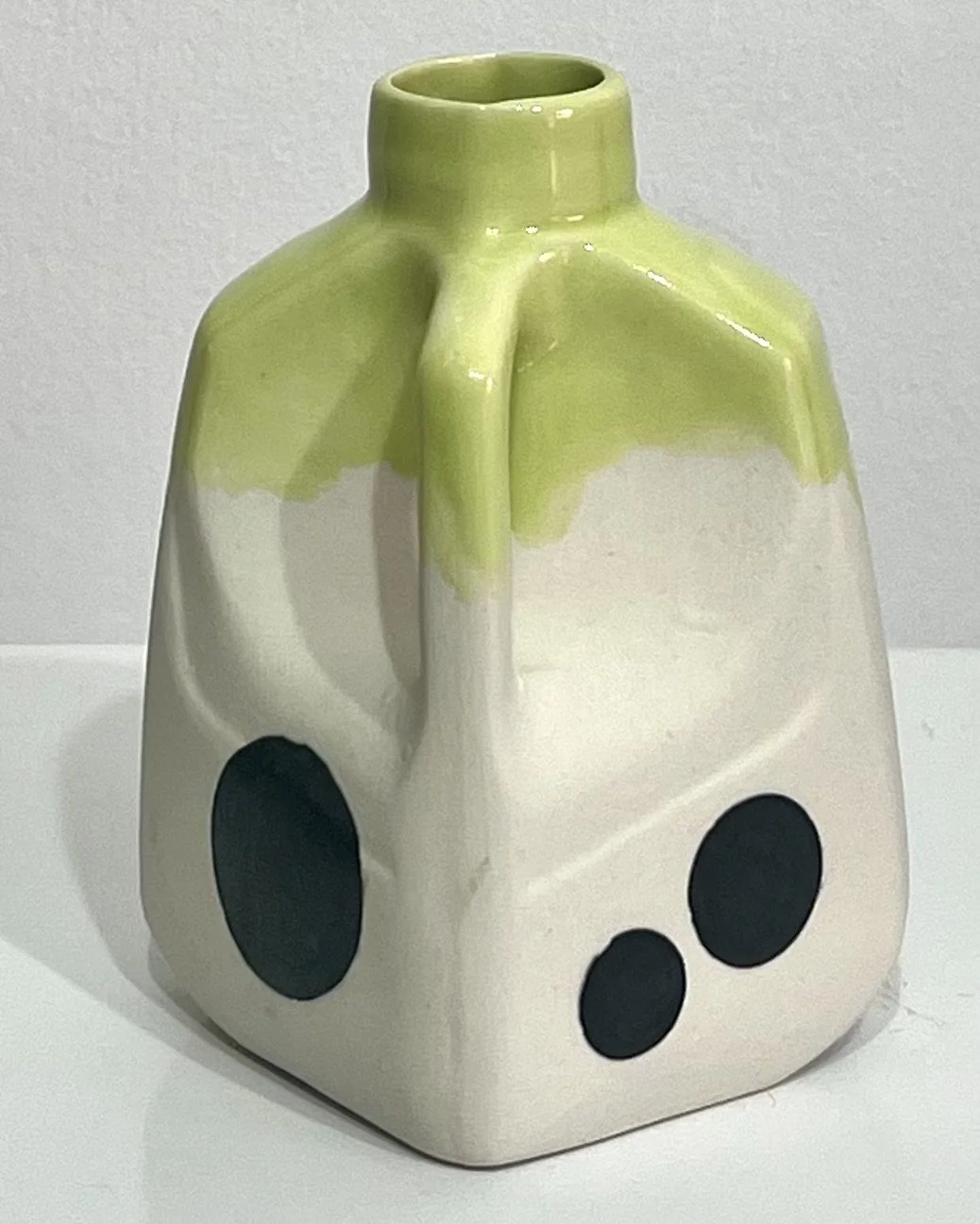 Angled view of porcelain milk jug No. 26.150 with the handle to the right, showing black polka dots and glossy lime-green glaze flowing over the shoulders.
