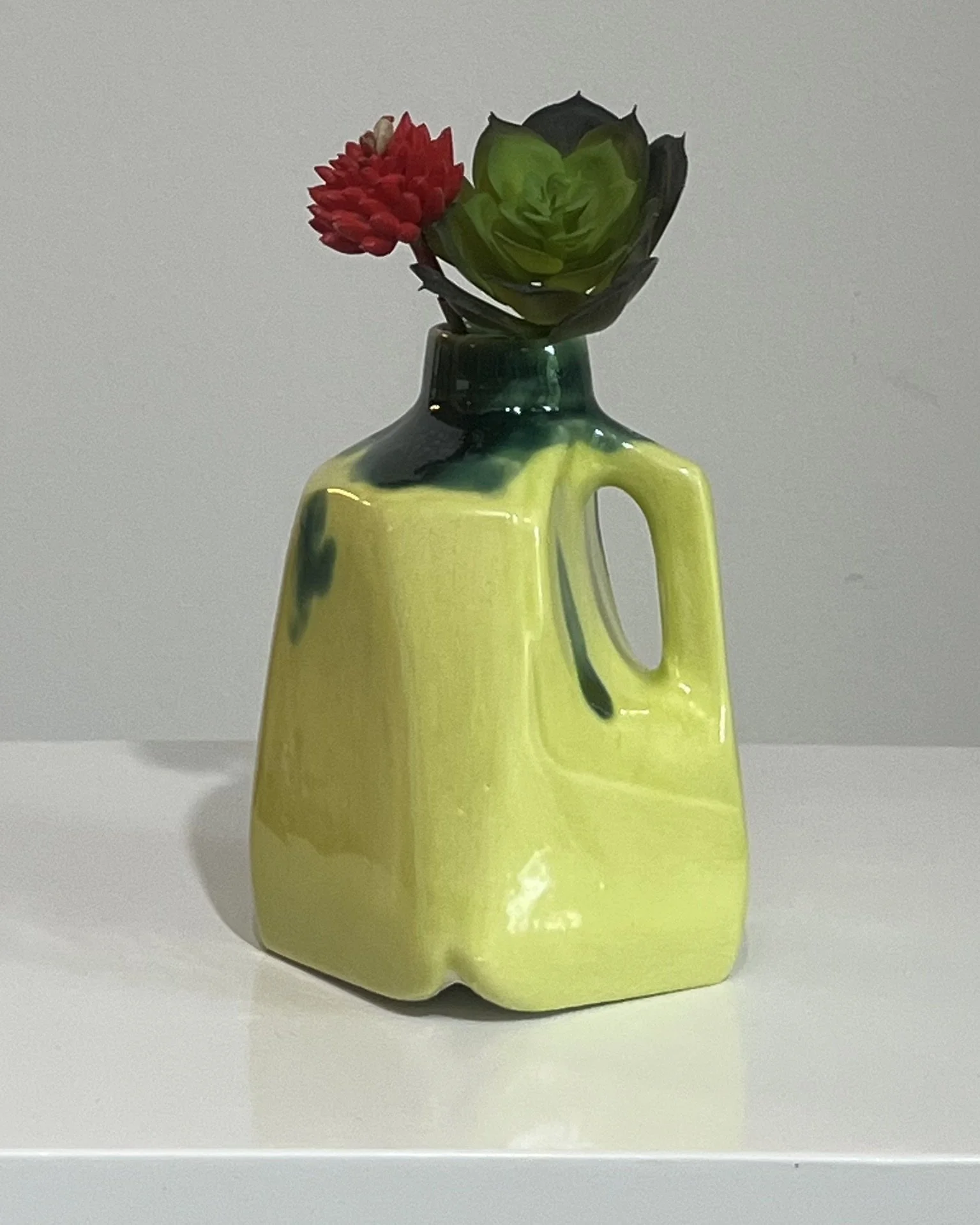 Handmade porcelain milk jug ceramic vase with lime green and dark green glazes displayed with a single red flower.