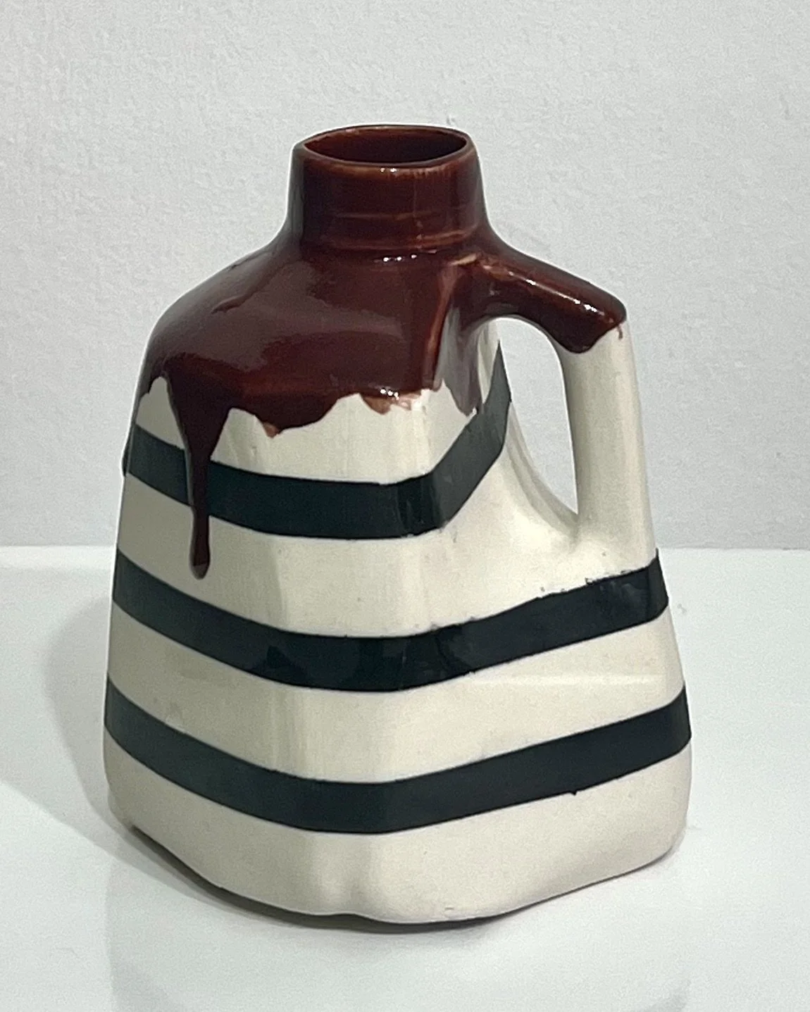 Front view of handmade porcelain milk jug No. 26.141 by Alissa Van Atta, featuring bold black horizontal stripes, a creamy white body, and glossy reddish-brown Deep Firebrick glaze.