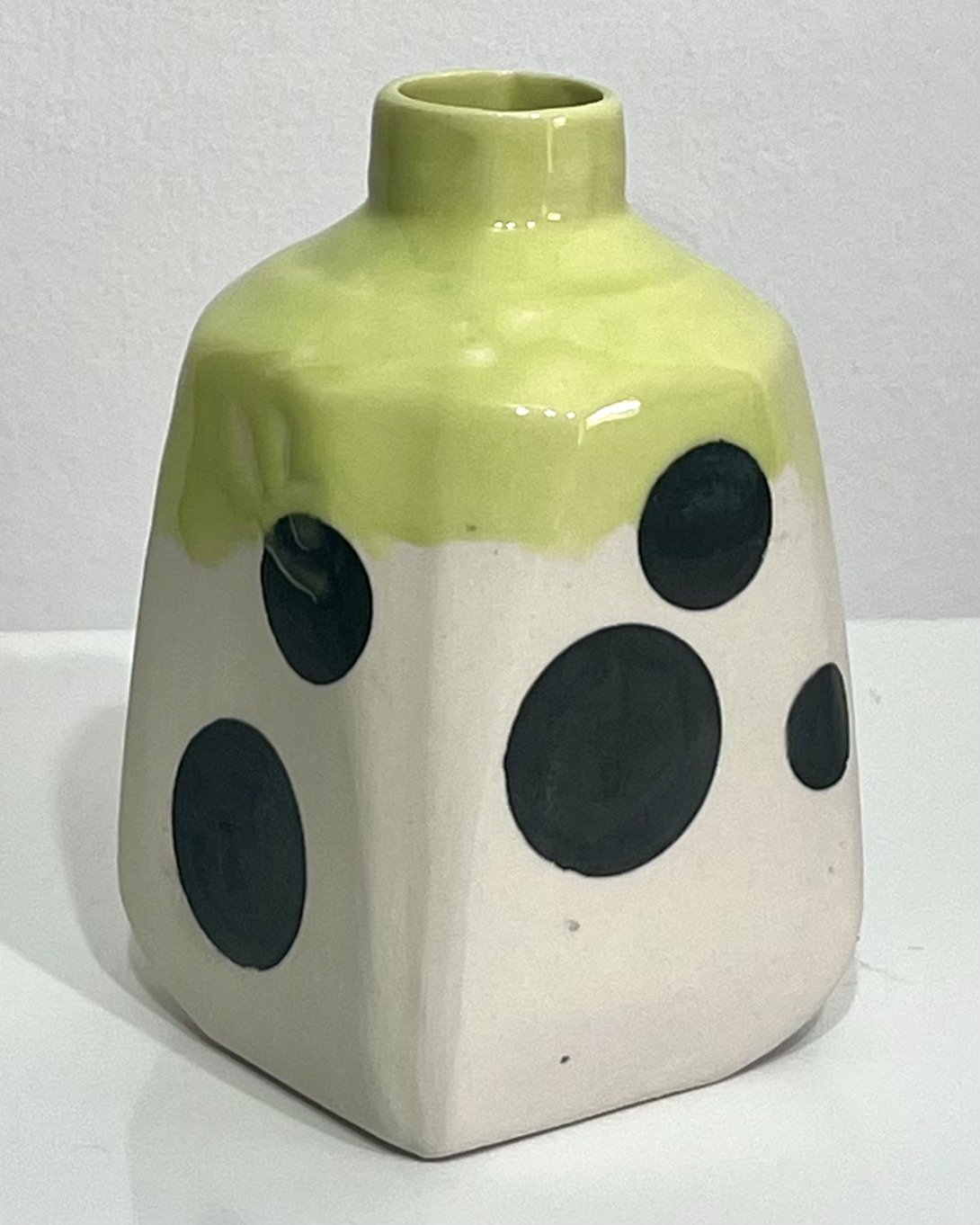 Side view of handmade polka dot porcelain milk jug No. 26.150, showing its compact handle, irregular black spots, and vivid Pear glazed neck.