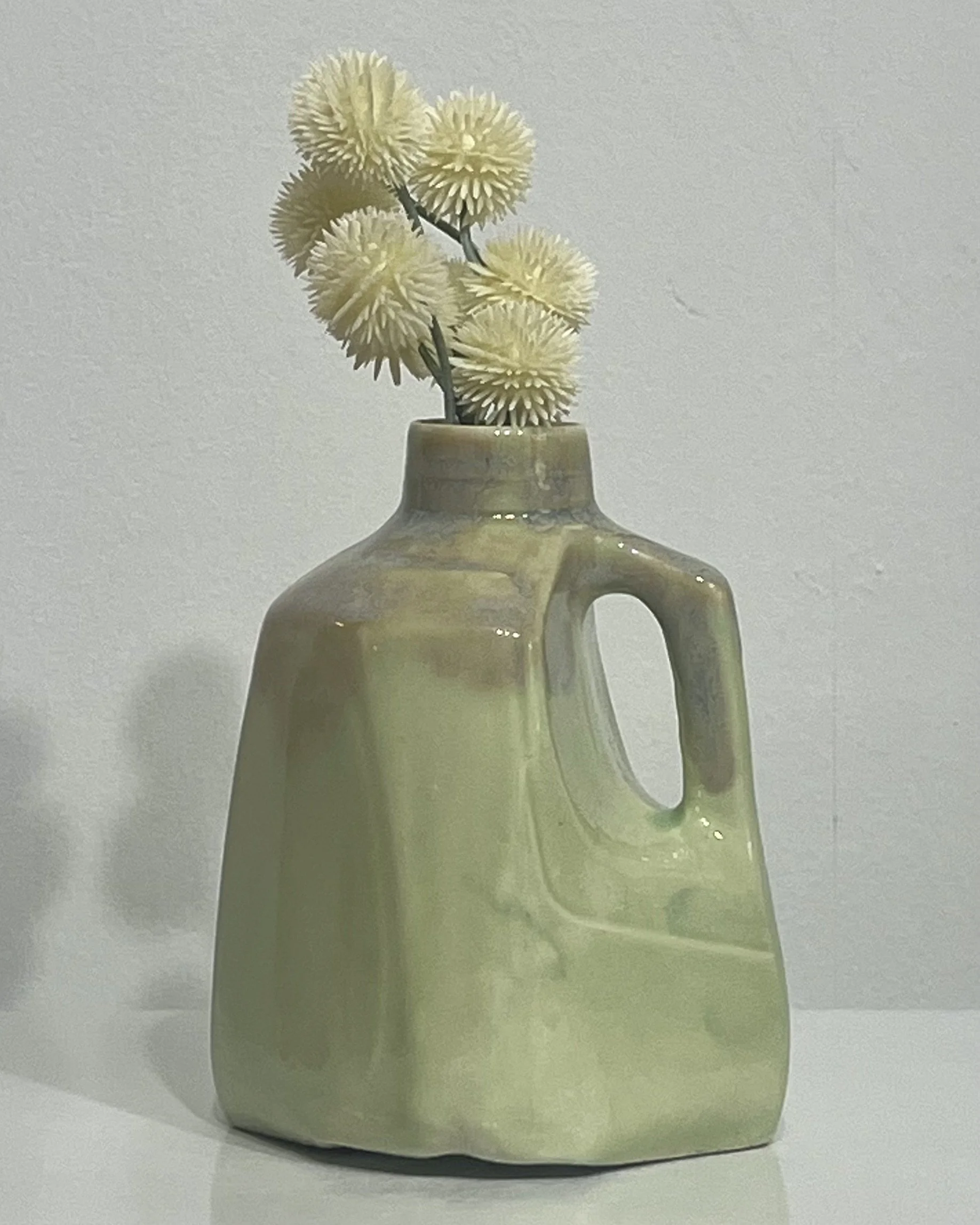 Handmade pale green porcelain milk jug by Alissa Van Atta, featuring Saguaro and Opal Lustre glazes, displayed with flowers.