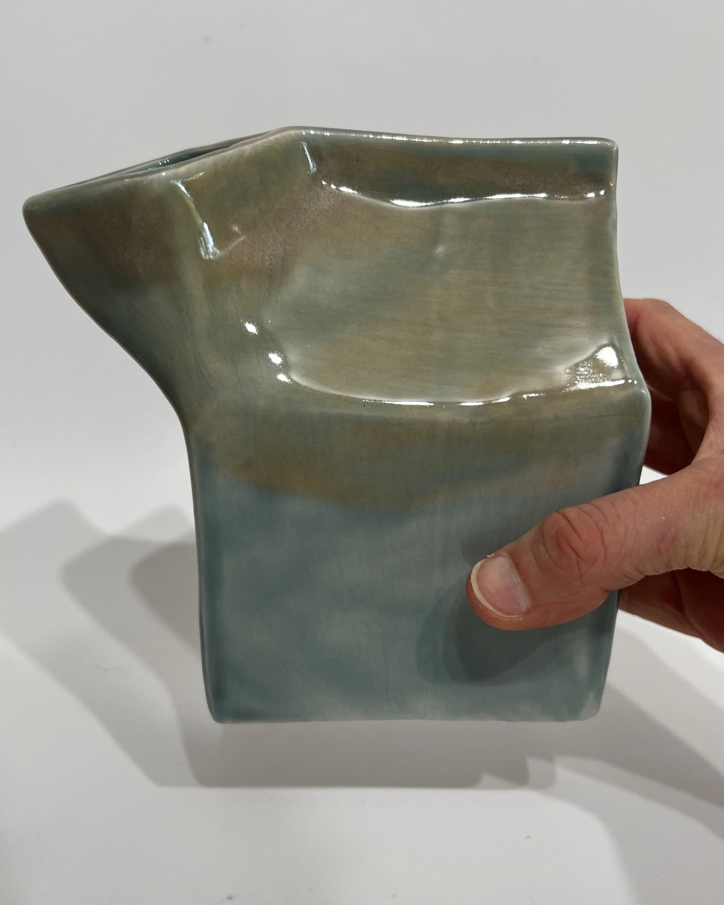 Hand holding ceramic milk carton to show the scale and handmade form.