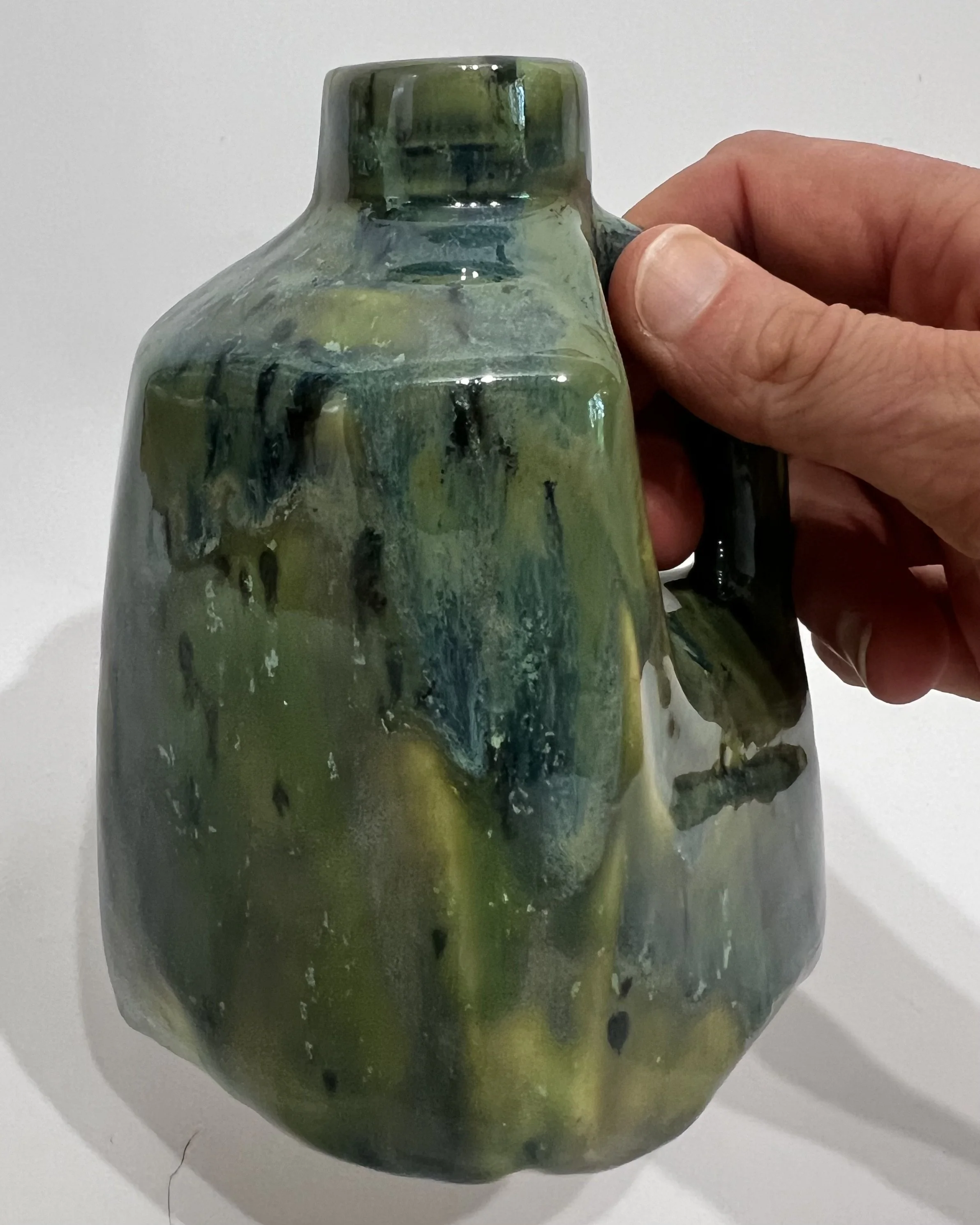 Hand holding a small green and blue porcelain milk jug to demonstrate its size and proportions.