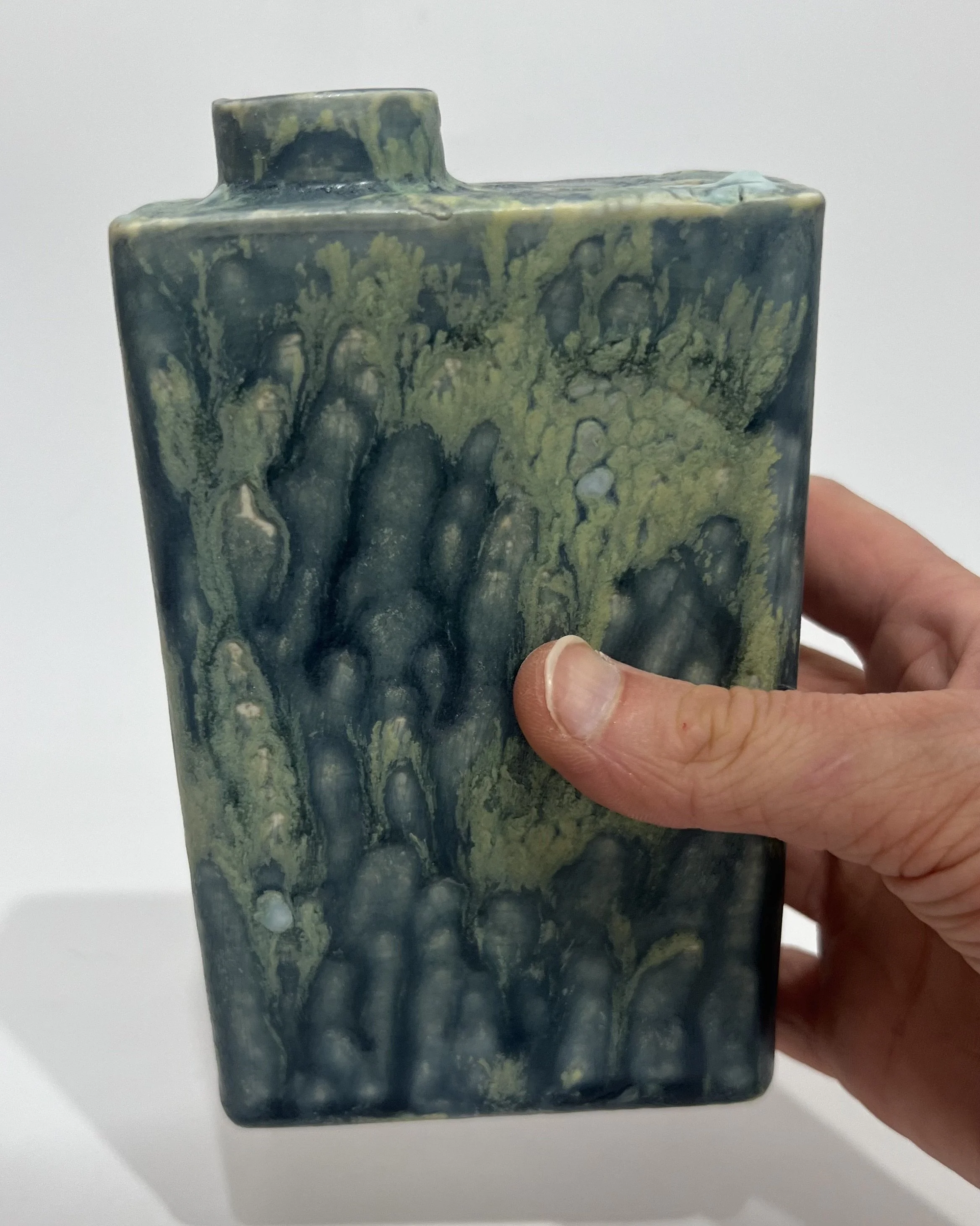 Hand holding a small, sculptural porcelain Carton vessel to demonstrate its dimensions.