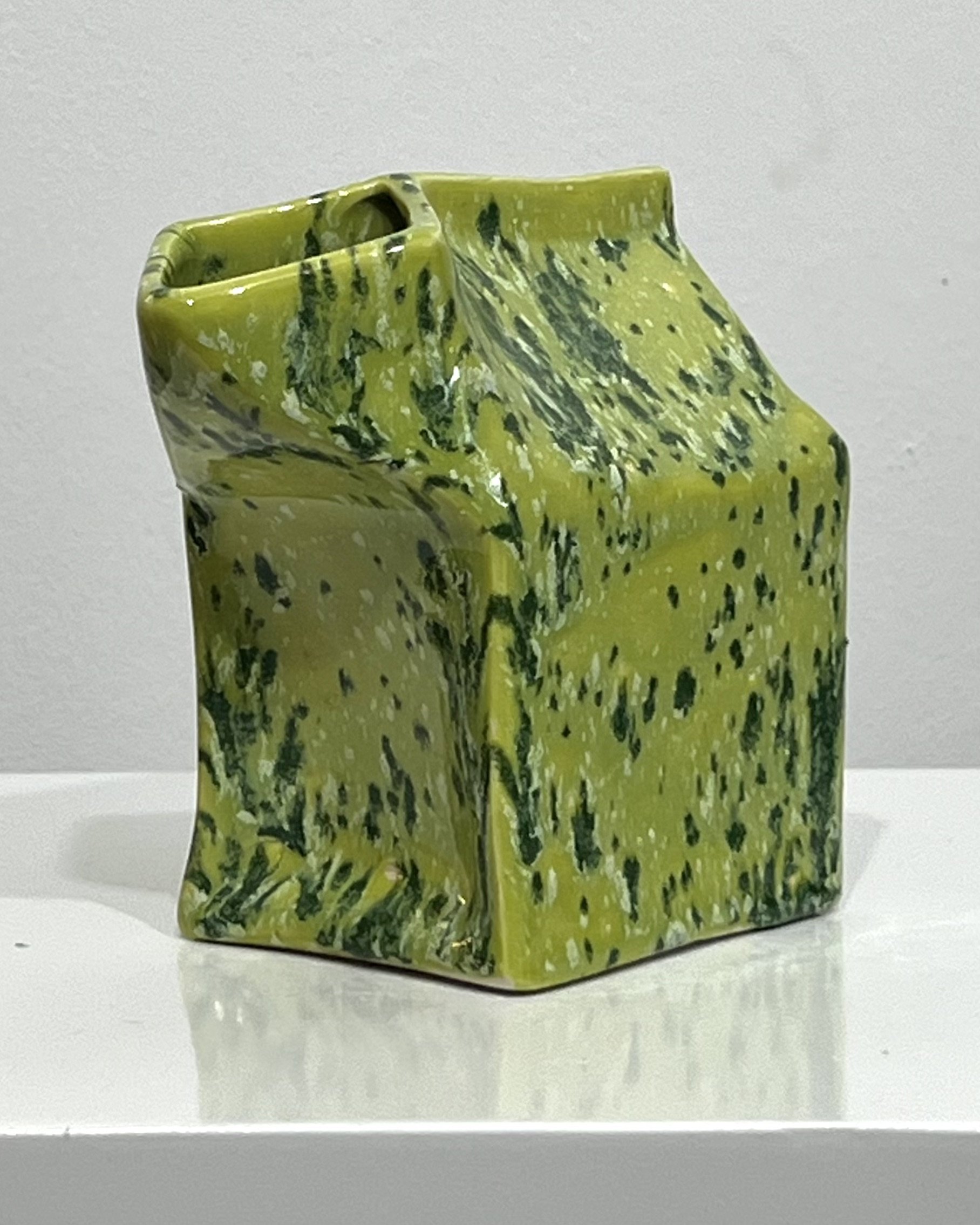 Handmade porcelain milk carton sculpture in Lime Shower glaze featuring chartreuse green and dark green speckled surface, shown as a contemporary ceramic art object.