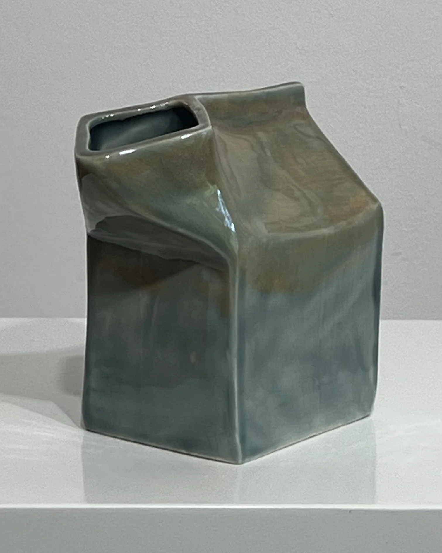 Handmade ceramic milk carton shown at an angle, with muted blue-green and earthy glaze variation.