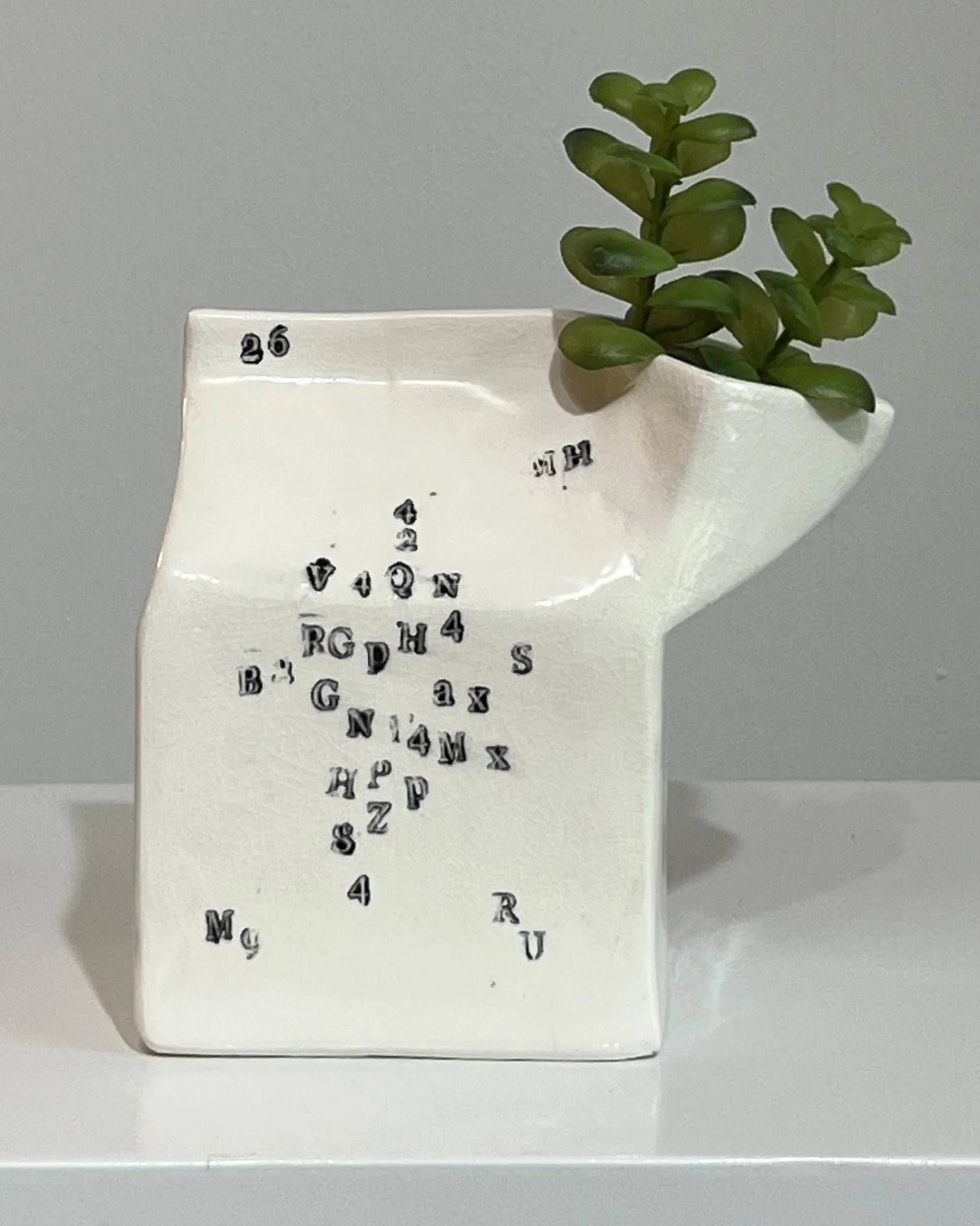 Handbuilt white porcelain milk carton from Alissa Van Atta's Type Series featuring black typographic impressions and green botanical stems.