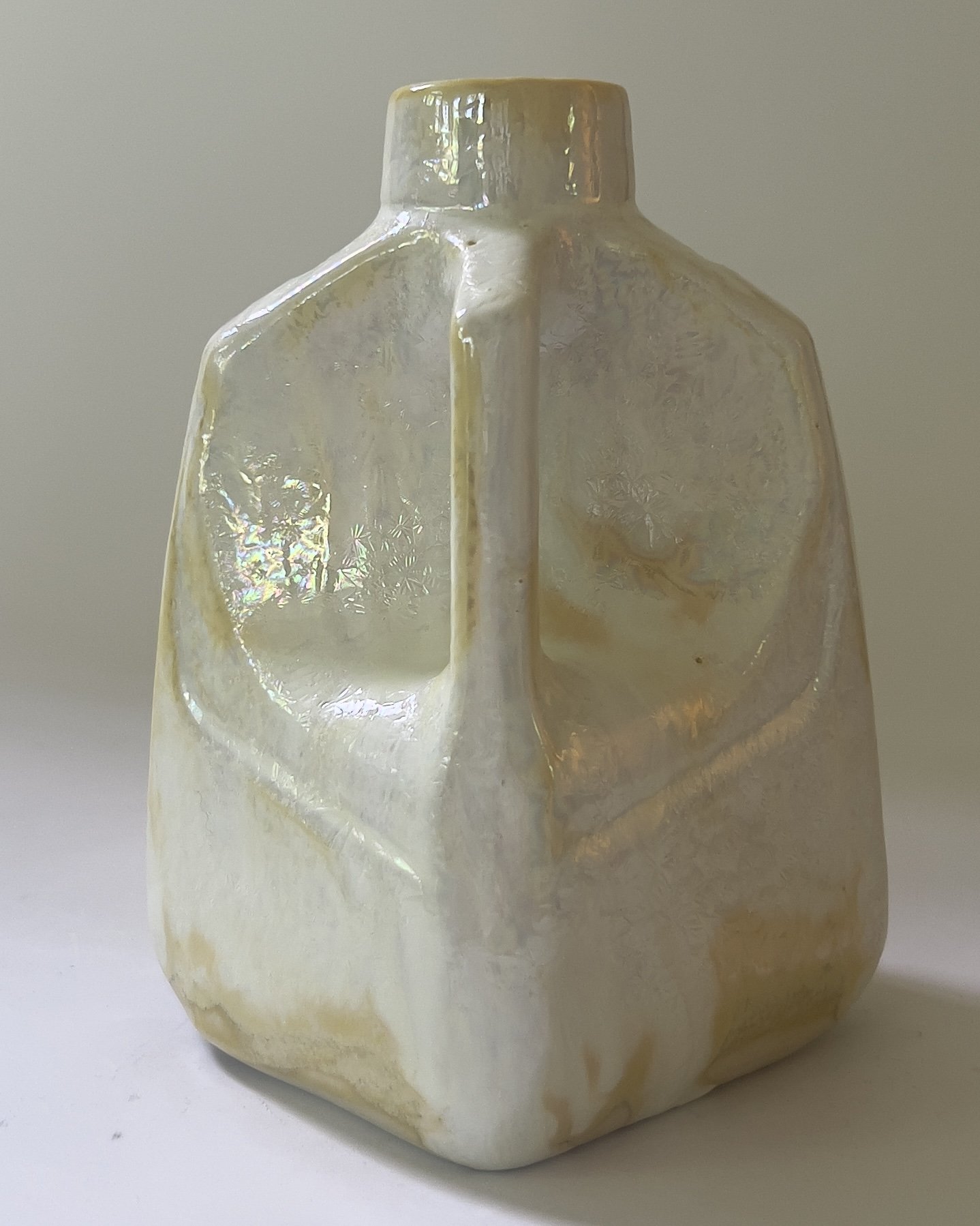 Side view of sculptural ceramic milk jug vase highlighting integrated handle and glossy iridescent surface