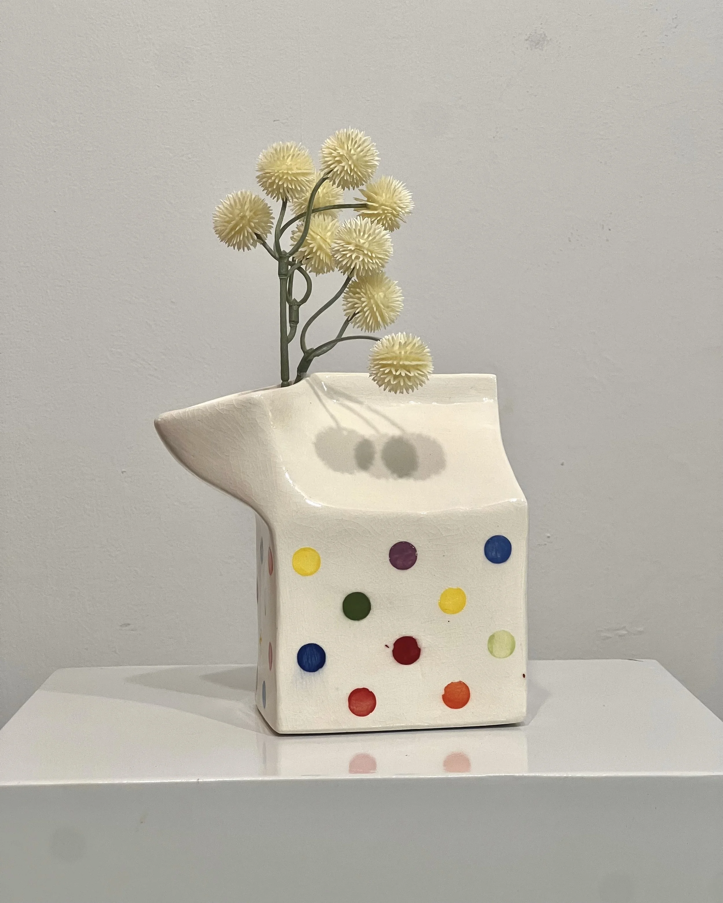 Handmade porcelain milk carton vessel with multicolored painted dots on a glossy white surface and folded carton-shaped top.