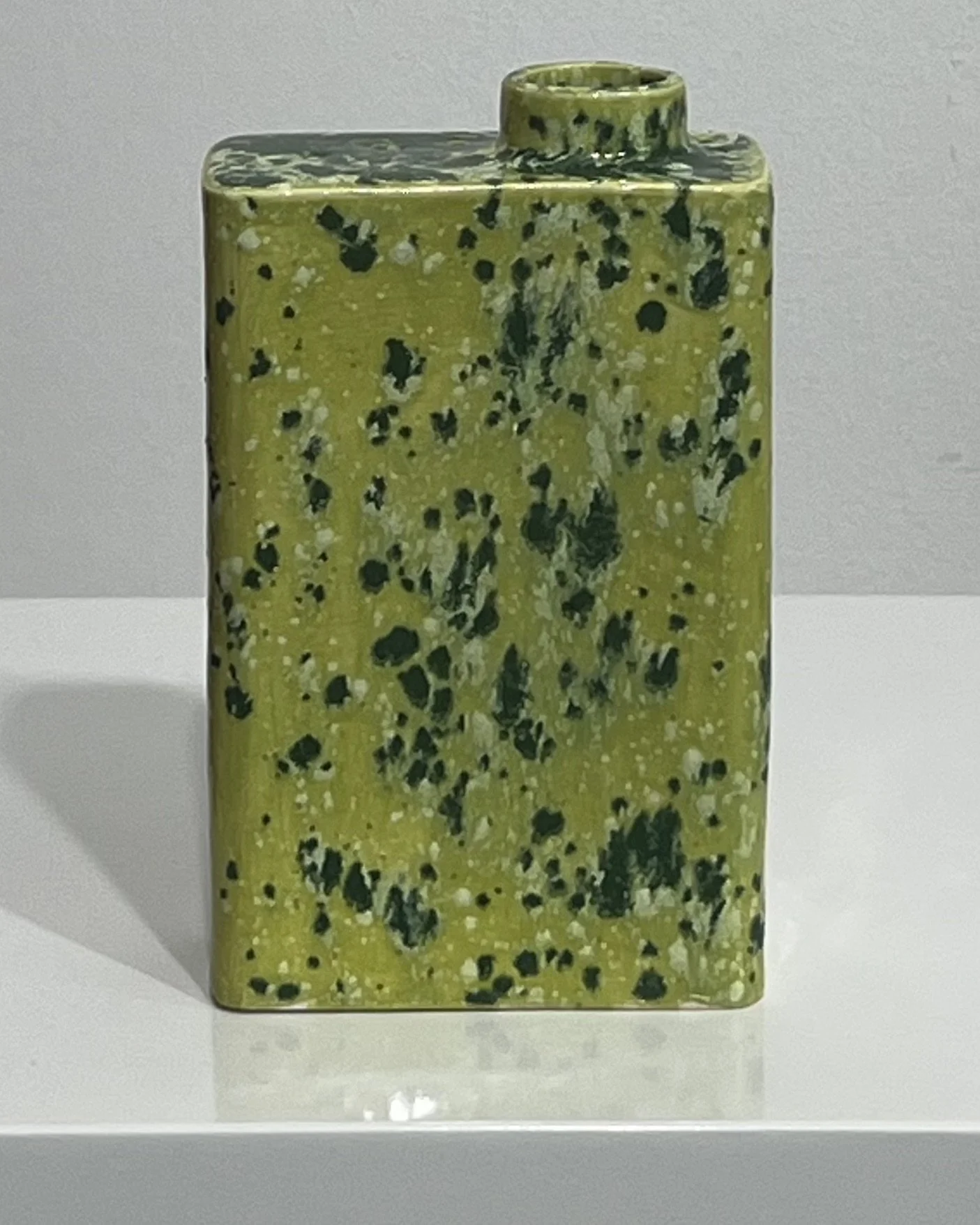 Back of sculptural green ceramic carton with dark speckles and irregular glaze patterns