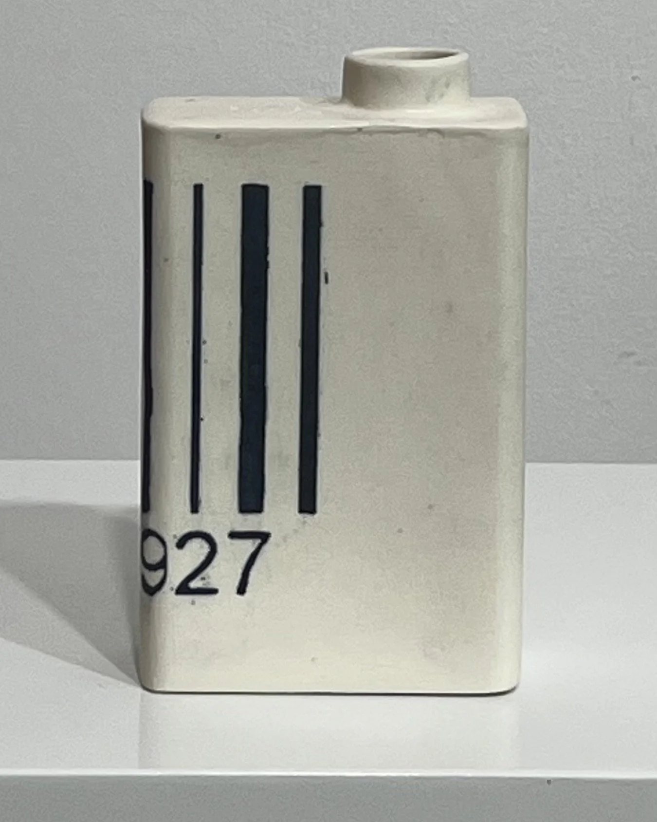 Side view of white porcelain milk carton with black barcode lines and hand-drawn numbers