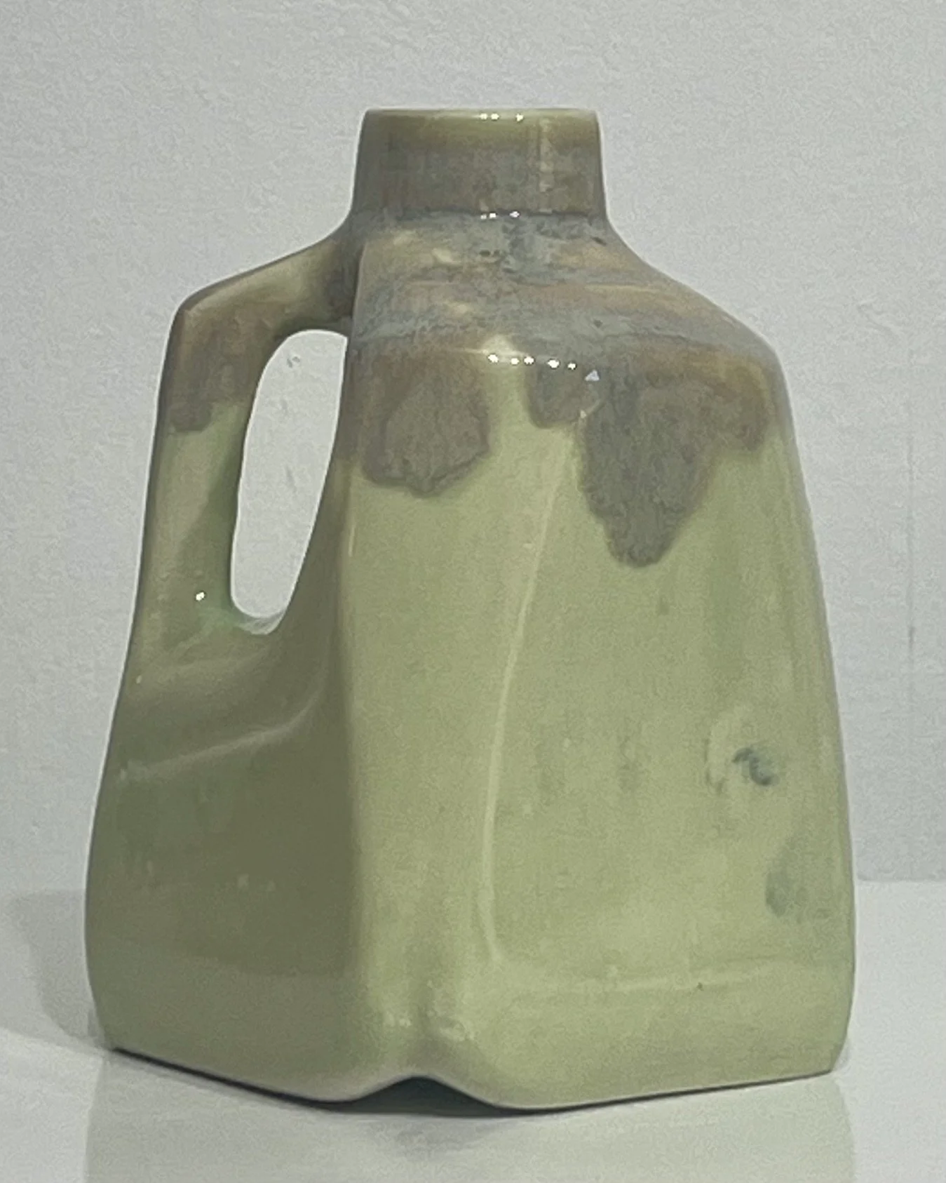 Back view of a light green handmade porcelain milk jug showing subtle variations in its glossy glaze.