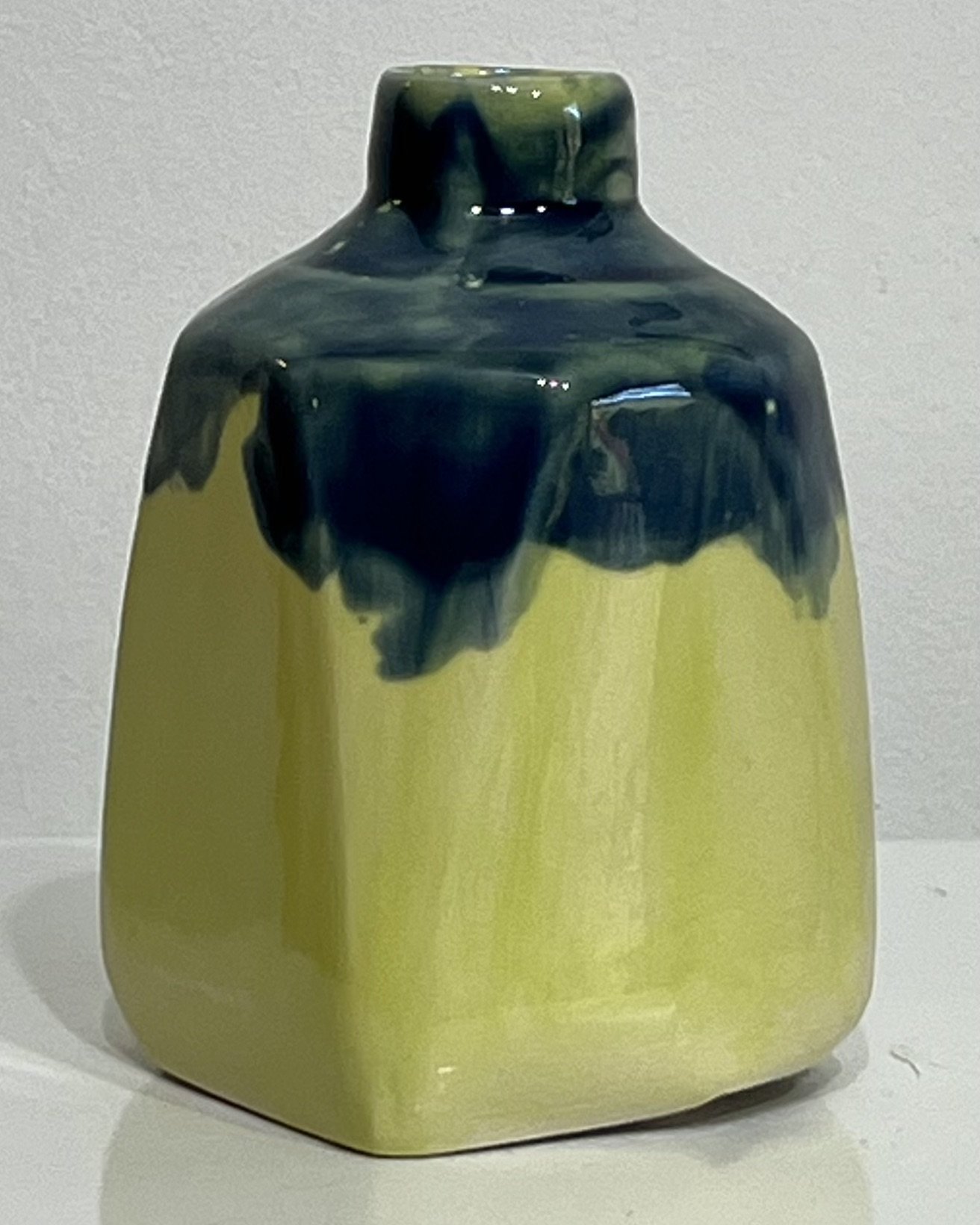 Left-side view of small handmade milk jug highlighting blue-green glaze flow and angular shoulders