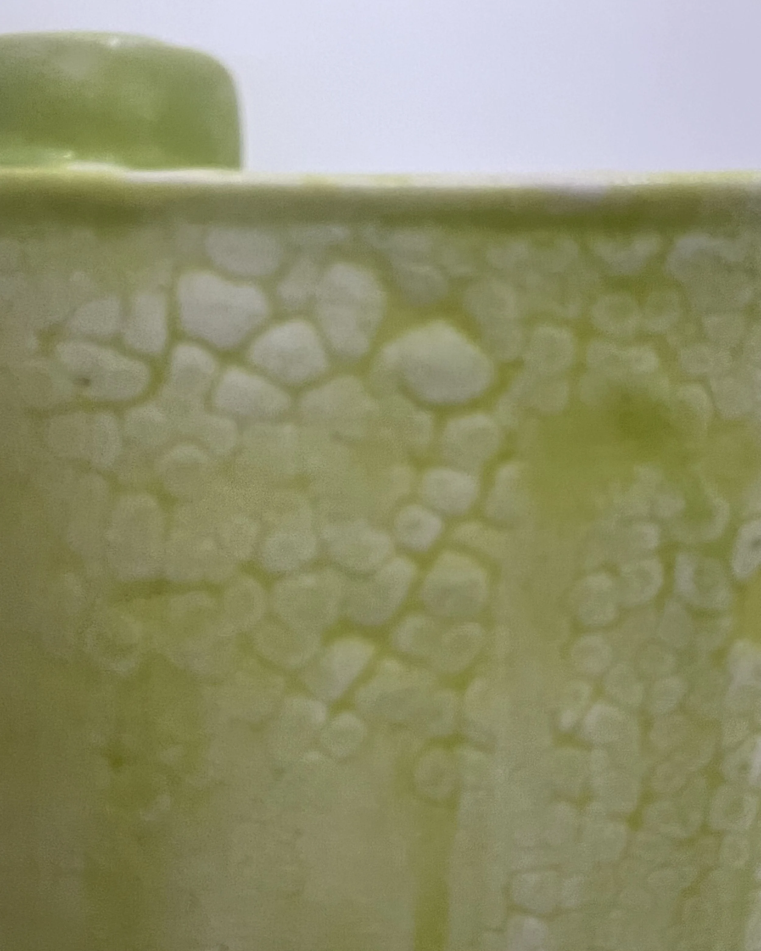 Close-up of Chartreuse and Mudcrack glaze interaction revealing mottled yellow-green and cream patterns on porcelain.