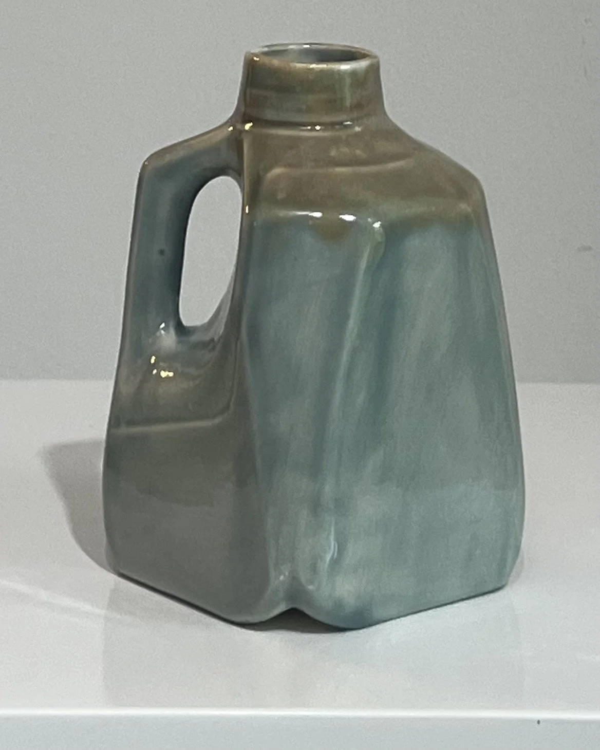 Opposite side of a handmade porcelain milk jug showing the layered blue-green glaze variation.