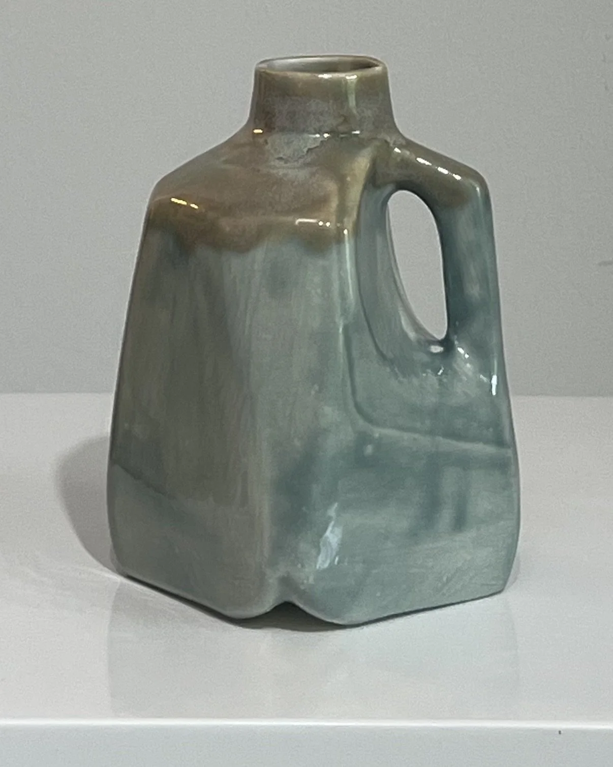Front view of a handmade porcelain milk jug with soft blue-green and satin white layered glazes.