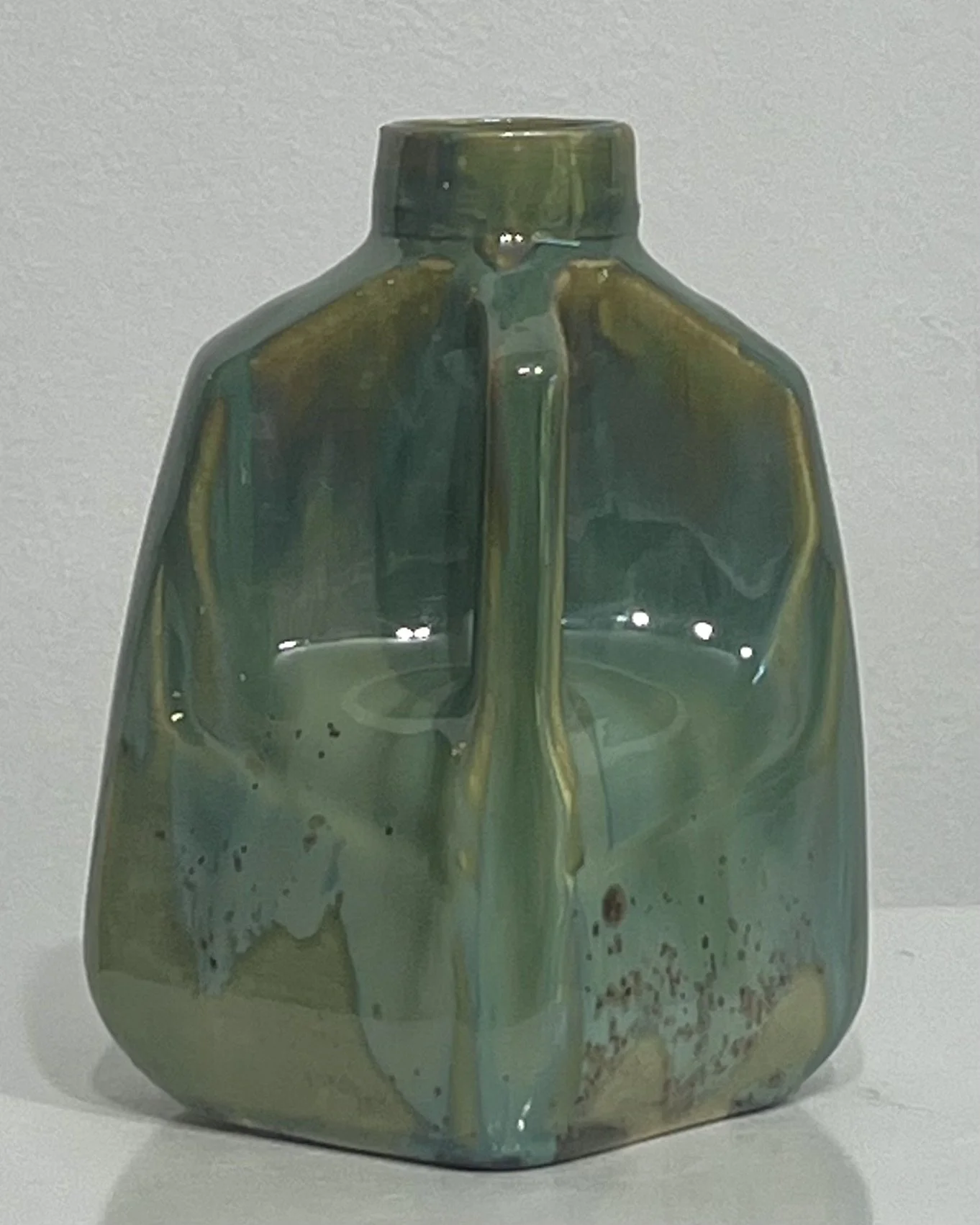 Right-side view of handmade porcelain milk jug with green layered glazes and sculptural handle.