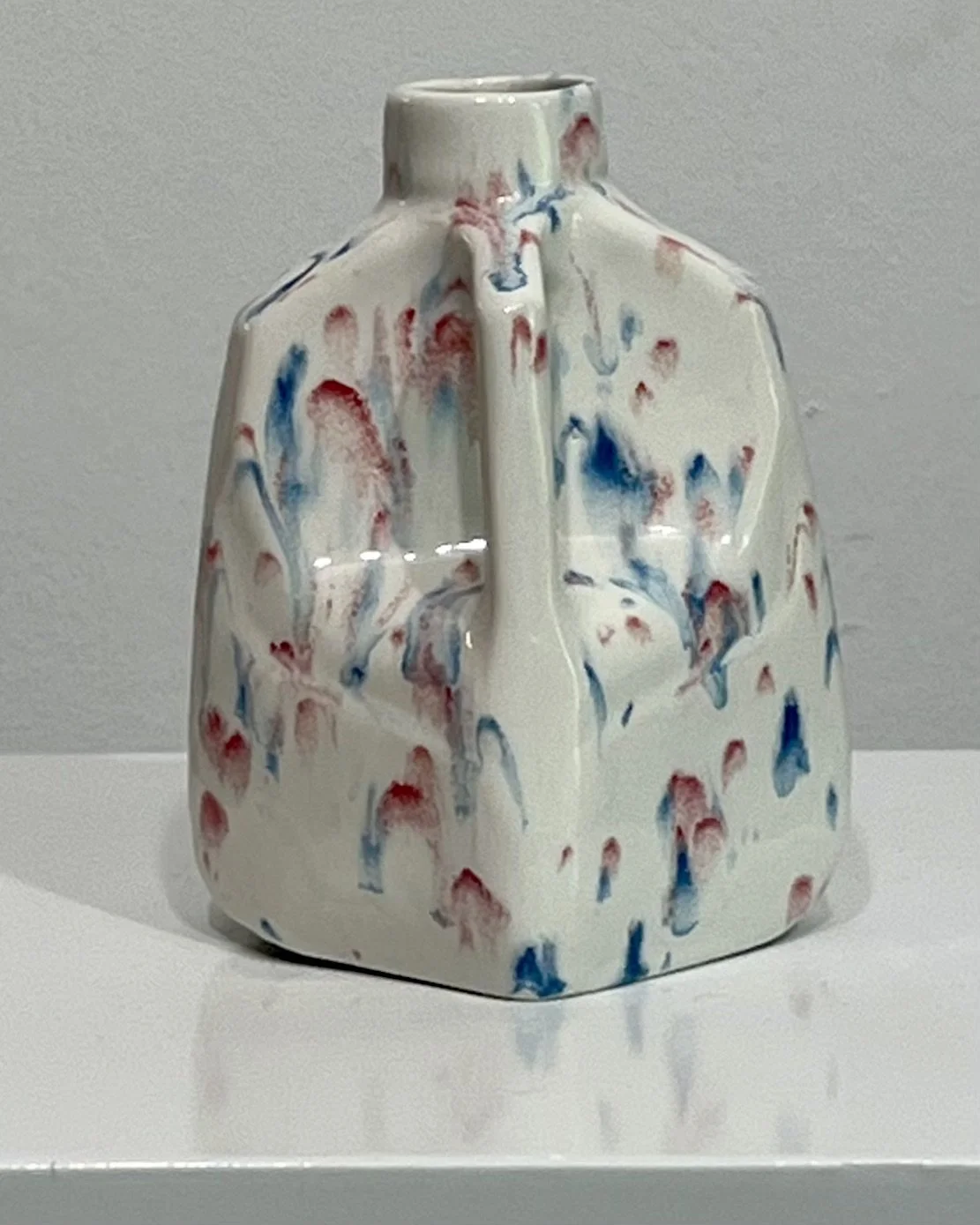 Close-up detail of red and blue splatter glaze on handmade porcelain milk jug vase.