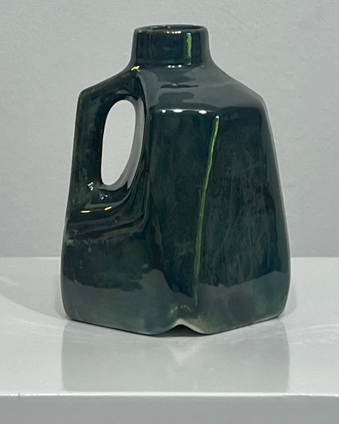 Three-quarter view of handmade porcelain milk jug vase showing sculptural form and layered green and bronze glaze.