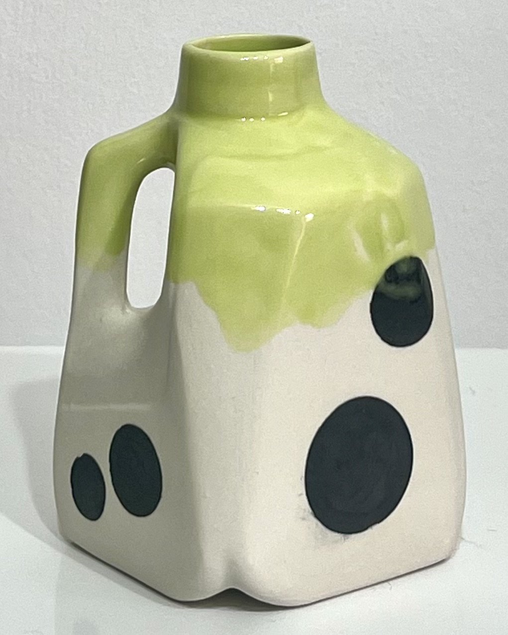 Back view of porcelain milk jug No. 26.150, with scattered black polka dots on the white body and yellow-green glaze over the upper section.