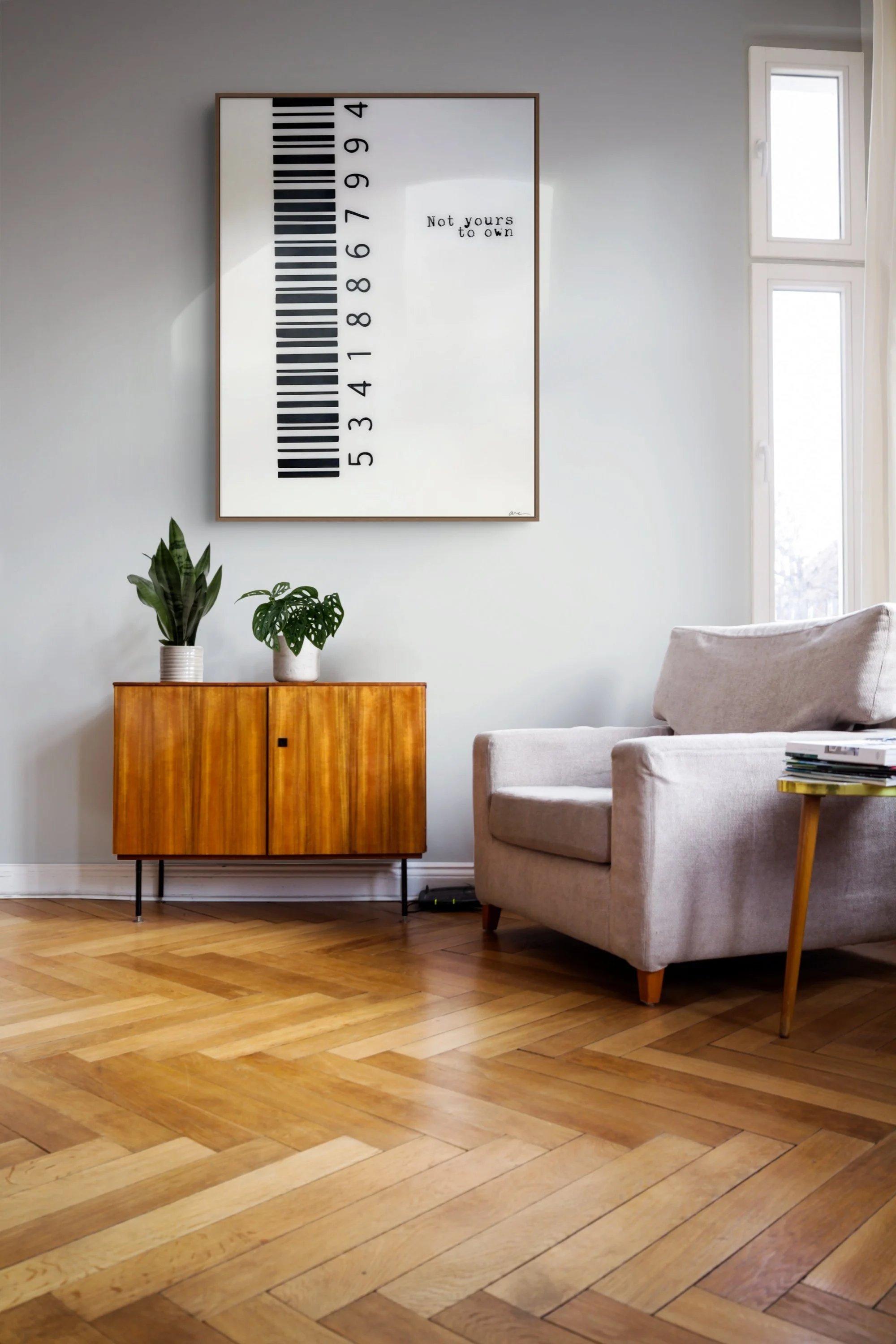 Large black-and-white Not Yours to Own barcode artwork by Alissa Van Atta displayed above a wooden credenza beside a contemporary upholstered chair.