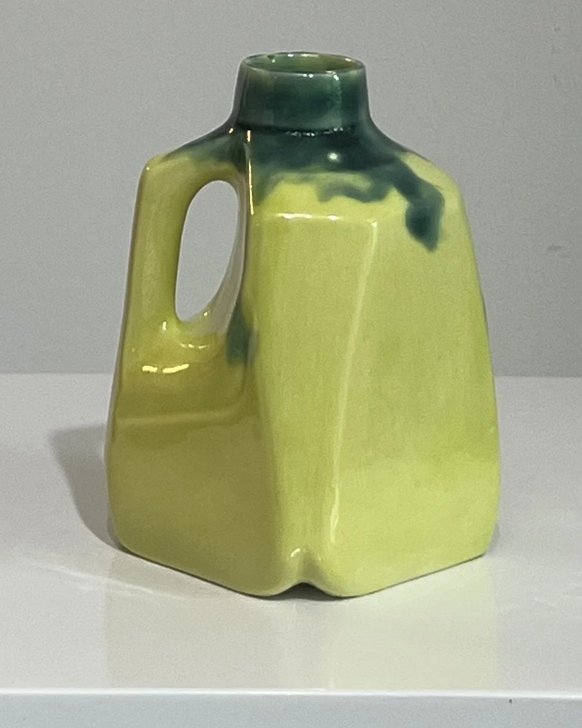 Back view of a handmade porcelain milk jug finished in lime green and dark green glazes.