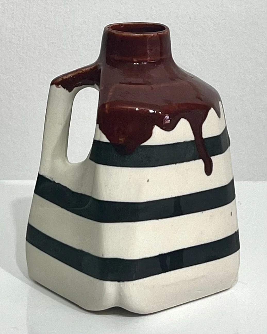 Back view of black-and-white striped porcelain milk jug No. 26.141 by Alissa Van Atta, showing the irregular Deep Firebrick glaze drips across its shoulders.