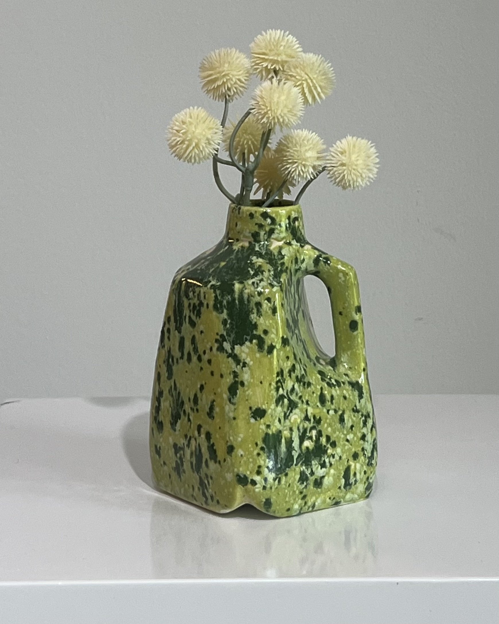 Handmade porcelain milk jug ceramic vase with a green speckled glaze displayed with white flowers.