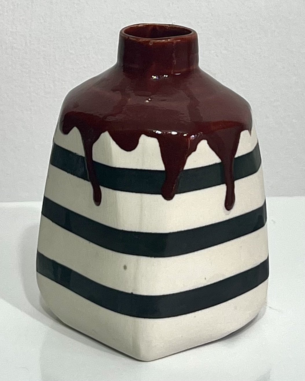 Side view of handcrafted striped porcelain milk jug No. 26.141, showing its curved handle, dark horizontal bands, and reddish-brown glaze drips.