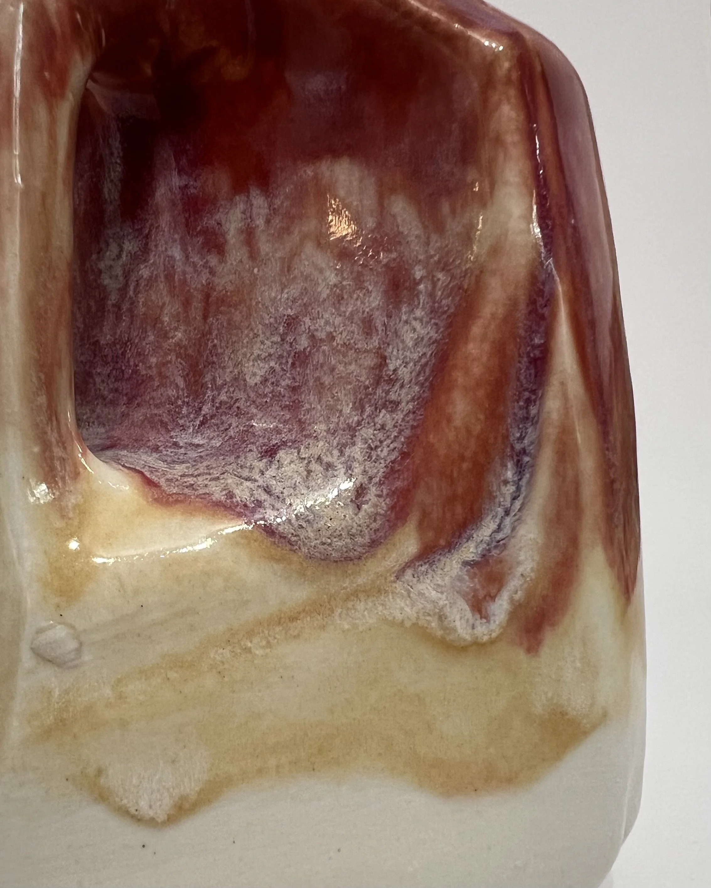 Close-up of plum, amber, and creamy ivory ceramic glazes flowing together on handmade porcelain