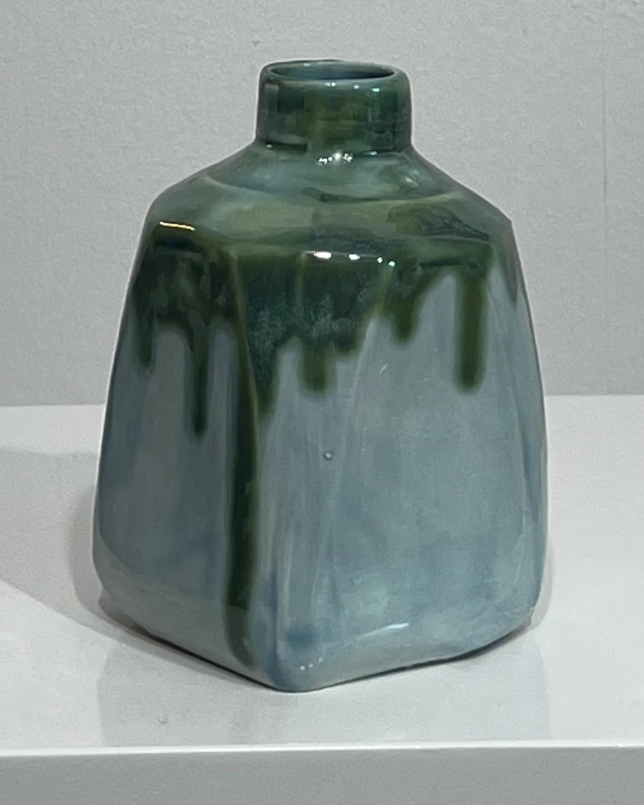 Back view of handbuilt ceramic milk jug vessel with glossy Seaweed glaze dripping over a pale blue-green surface.