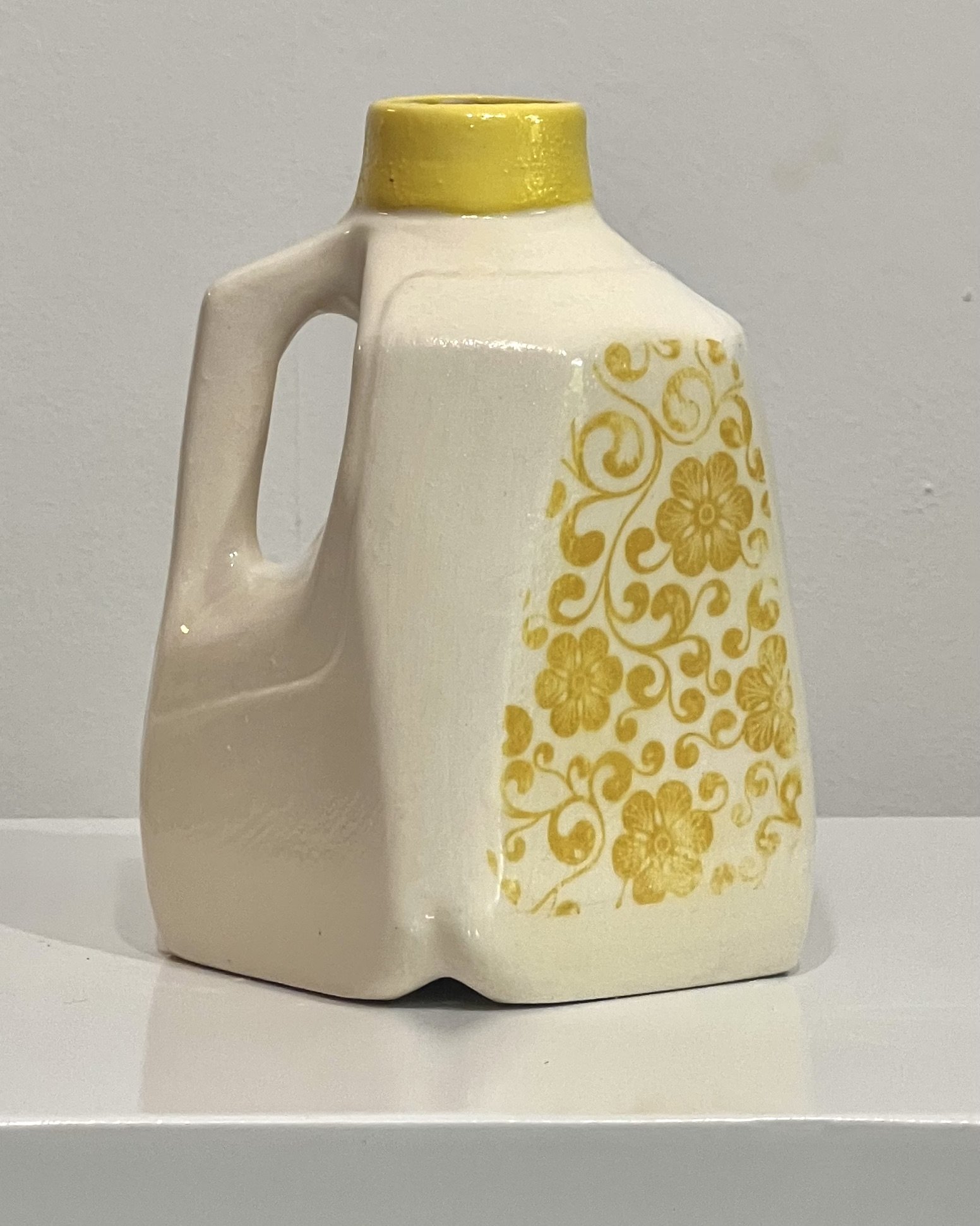 Right side view of a handcrafted yellow floral porcelain milk jug with glossy clear glaze.