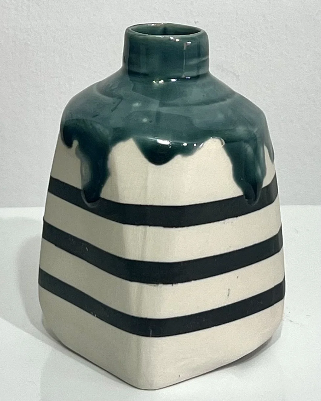 Left-handle view of handmade striped porcelain milk jug No. 26.142, showing its sculptural handle, contrasting black and white bands, and deep teal-green glaze.