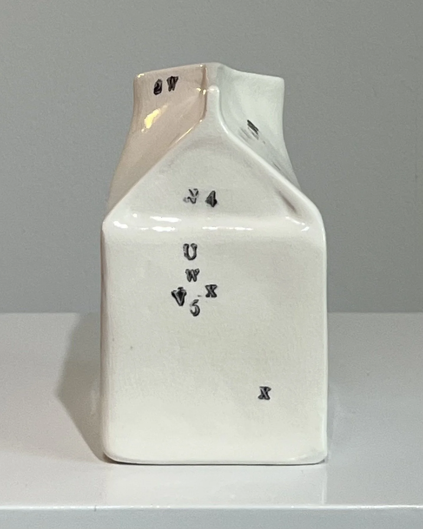 Left side view of a contemporary porcelain milk carton showing its sculptural profile and impressed typography.