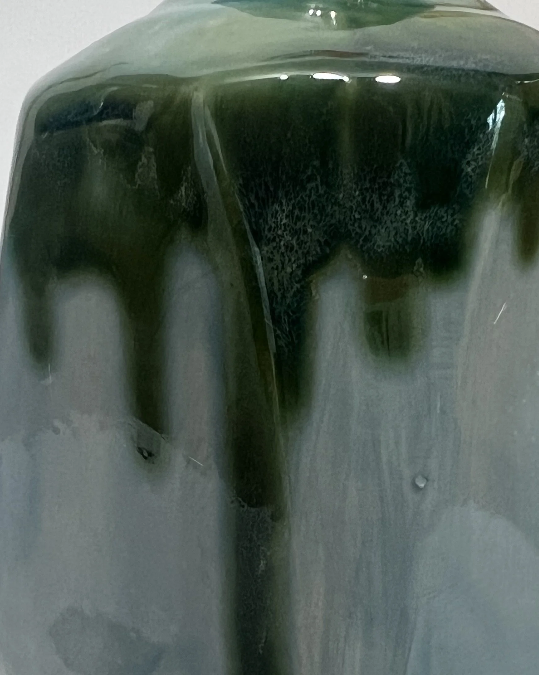 Close-up of glossy dark green Seaweed glaze dripping over soft blue-green Lagoon glaze on a handmade ceramic vessel.