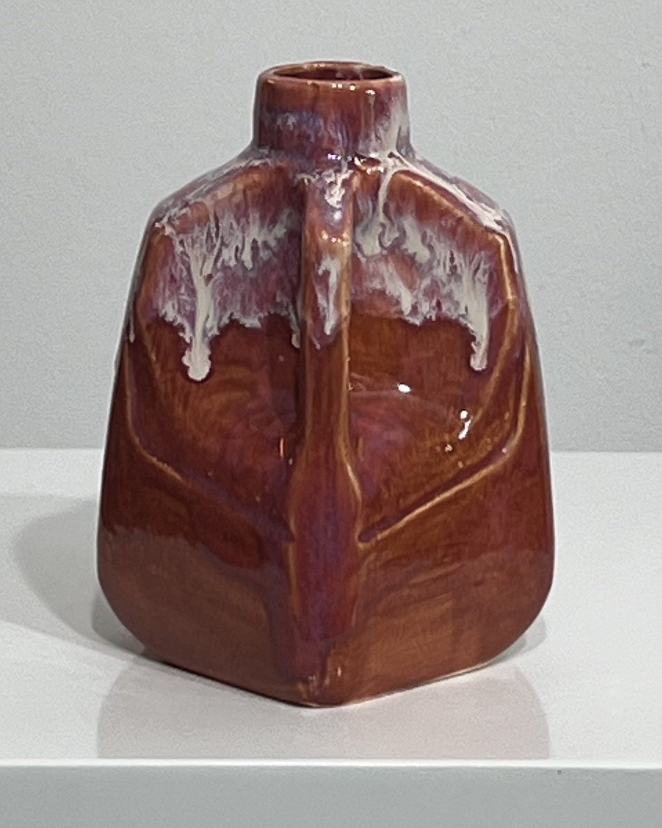 Angled view of handmade red ceramic milk jug showing geometric shape and handle