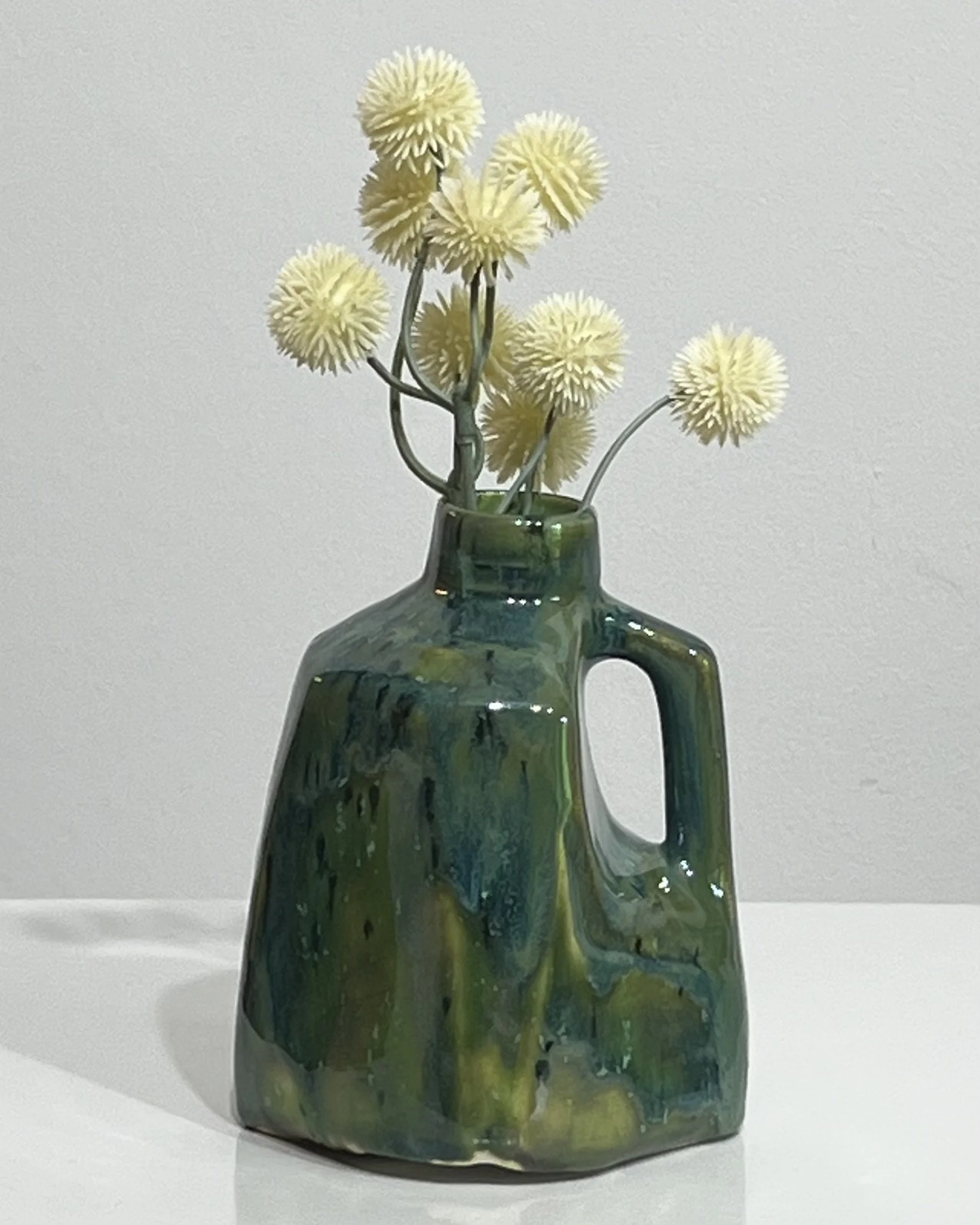 Handmade green and blue porcelain milk jug vase by Alissa Van Atta, styled with small yellow flowers.
