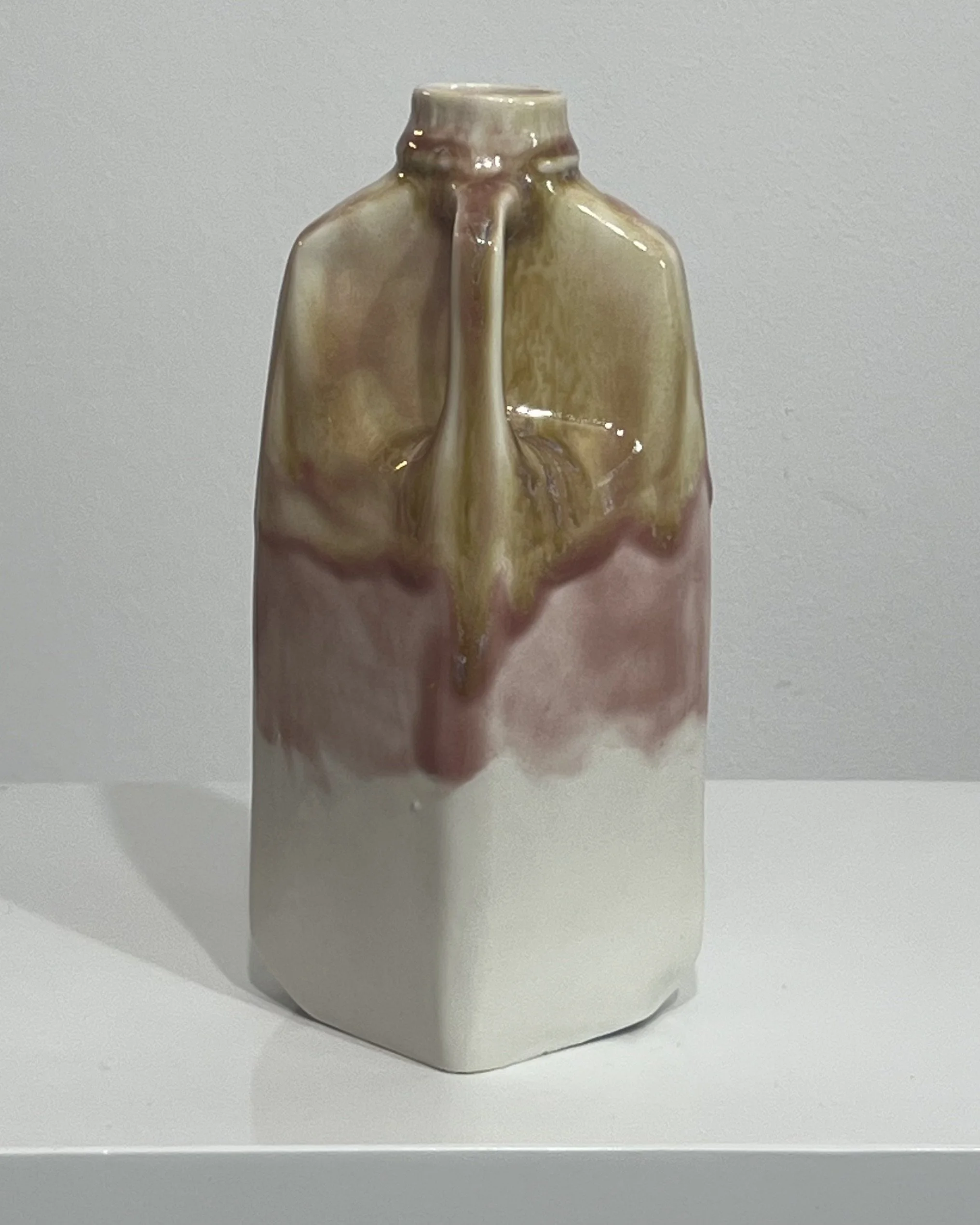 Angled view of one-of-a-kind tall ceramic milk jug with flowing olive green and blush pink glaze over a white base.