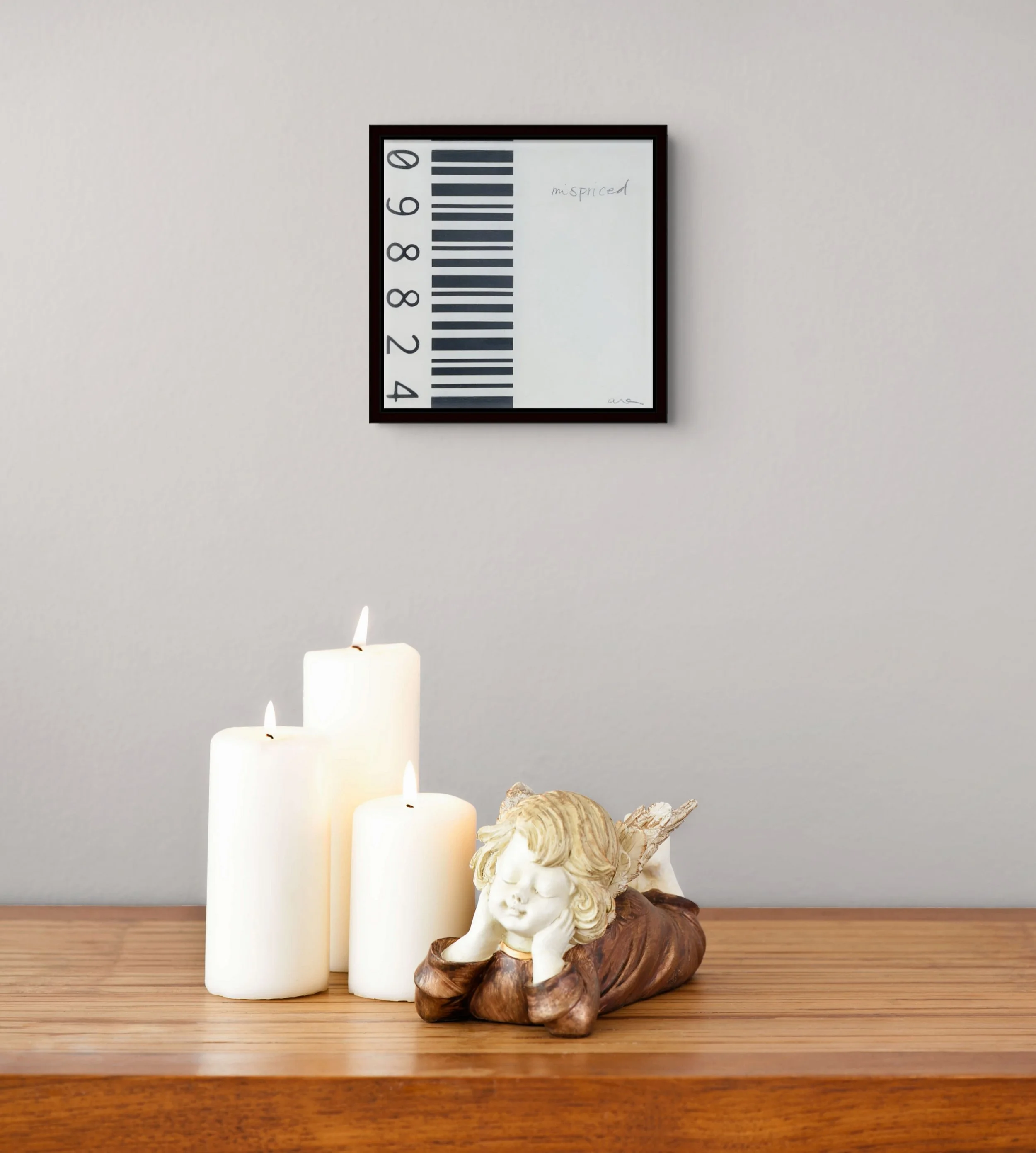 Mispriced, a small framed feminist barcode artwork by Alissa Van Atta, displayed on a neutral wall above a wooden console with candles and decorative objects.