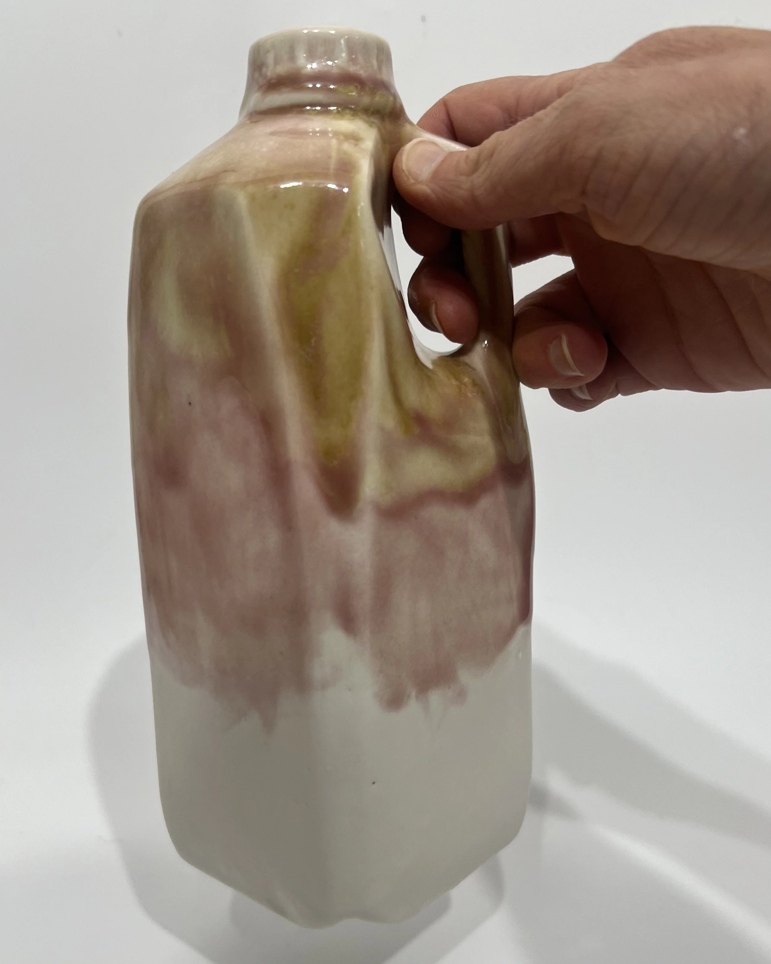 Tall ceramic milk jug held by the handle to show the scale and handmade sculptural form.