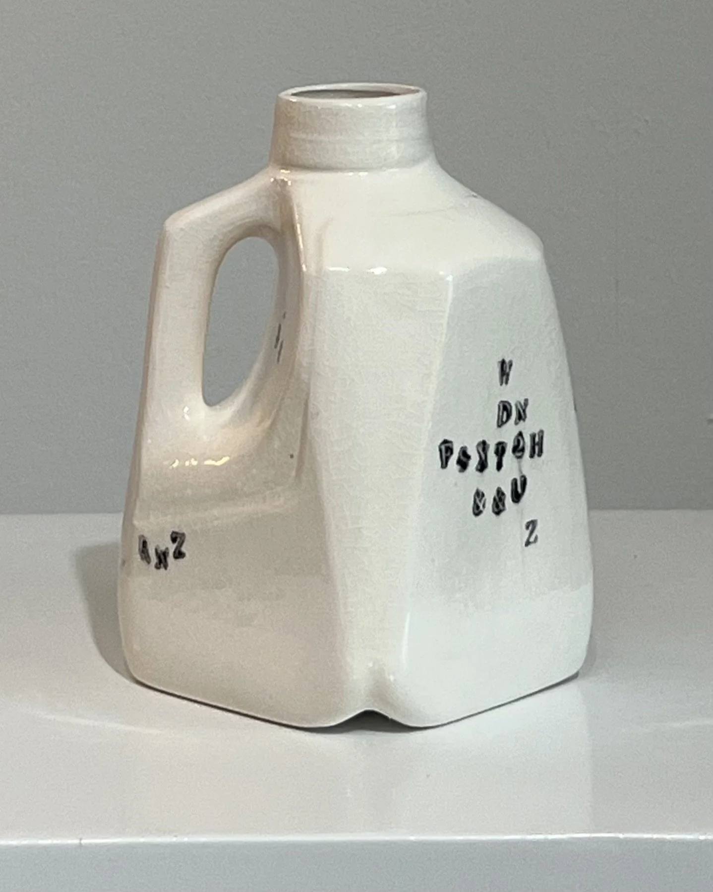 Rear view of a handbuilt porcelain milk jug showing the sculptural form and black typographic impressions.