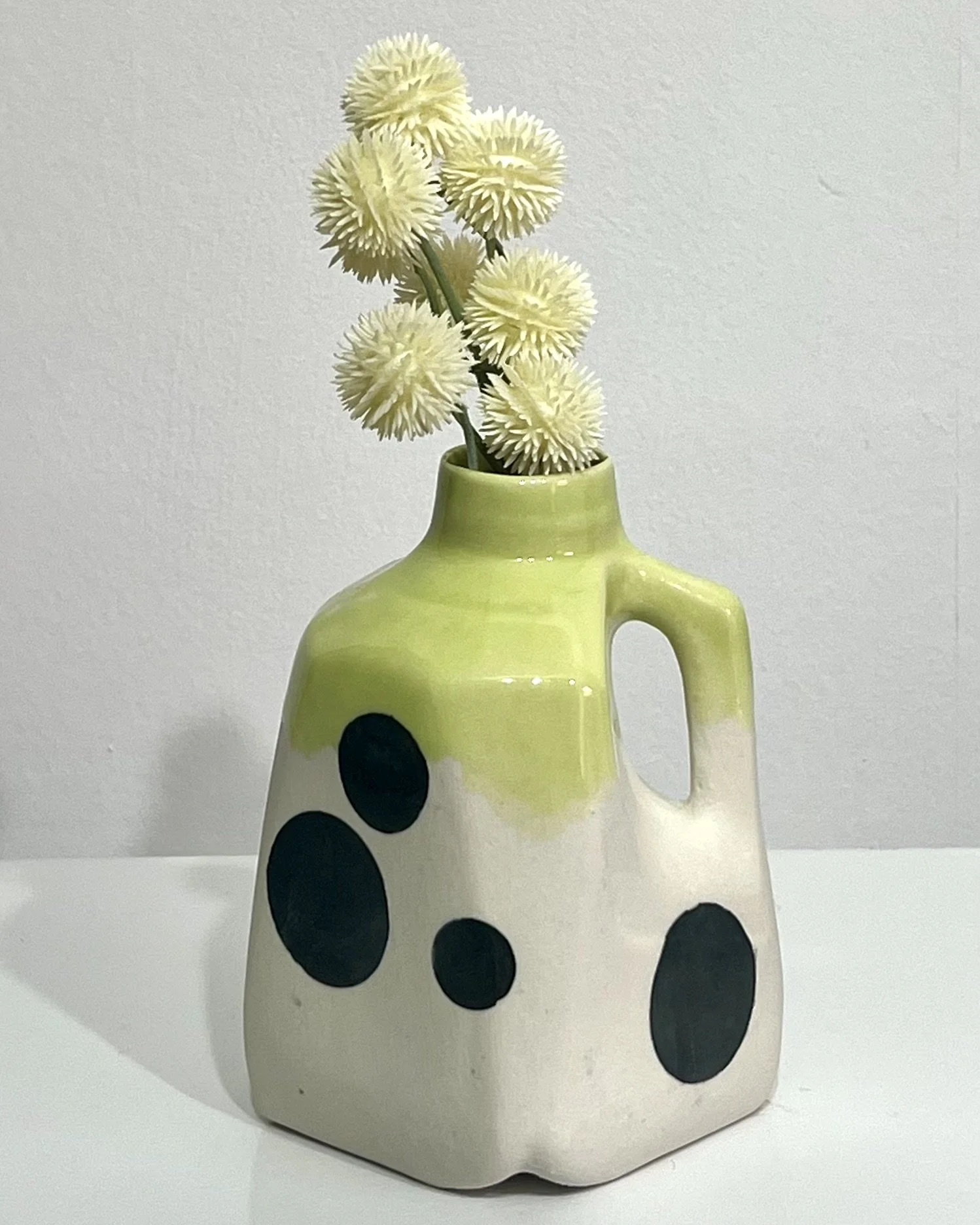 Polka dot porcelain milk jug No. 26.150 styled with pale botanical stems, featuring a bright chartreuse glazed top and bold black spots.