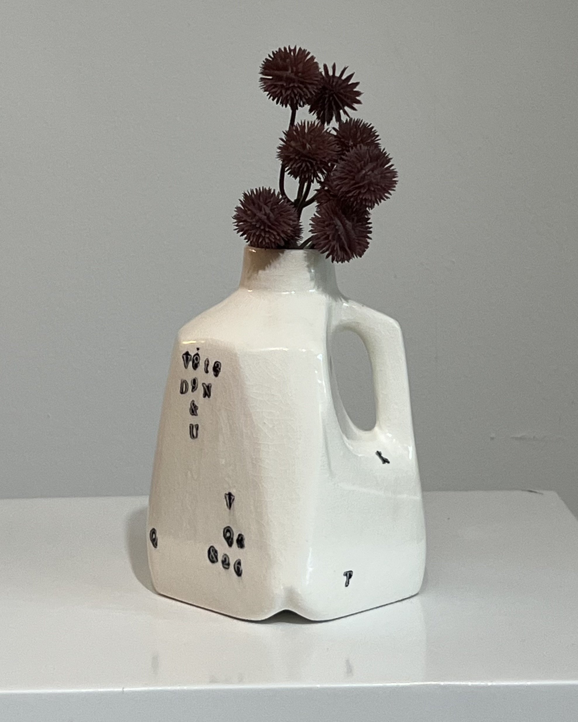 Handbuilt white porcelain milk jug from Alissa Van Atta's Type Series featuring black typographic impressions and burgundy botanical stems.