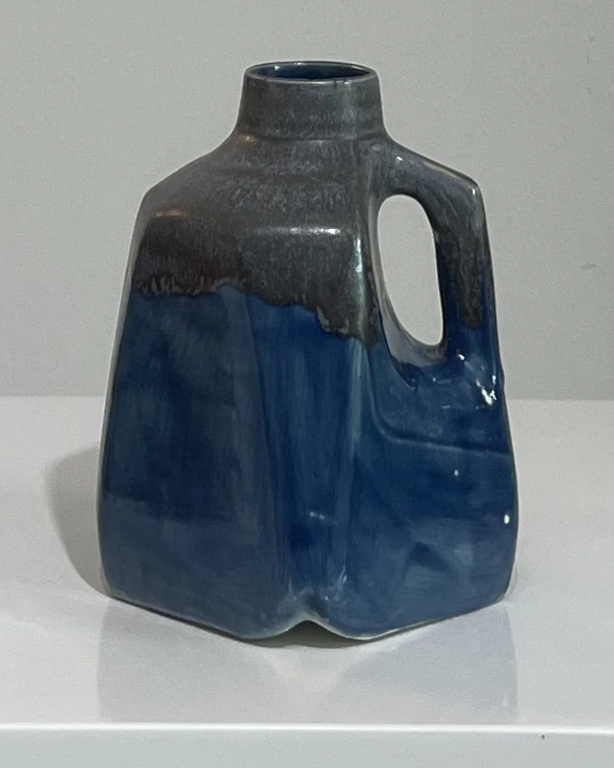 Front angled view of a handmade porcelain milk jug finished in layered cobalt blue and smoky gray glazes.