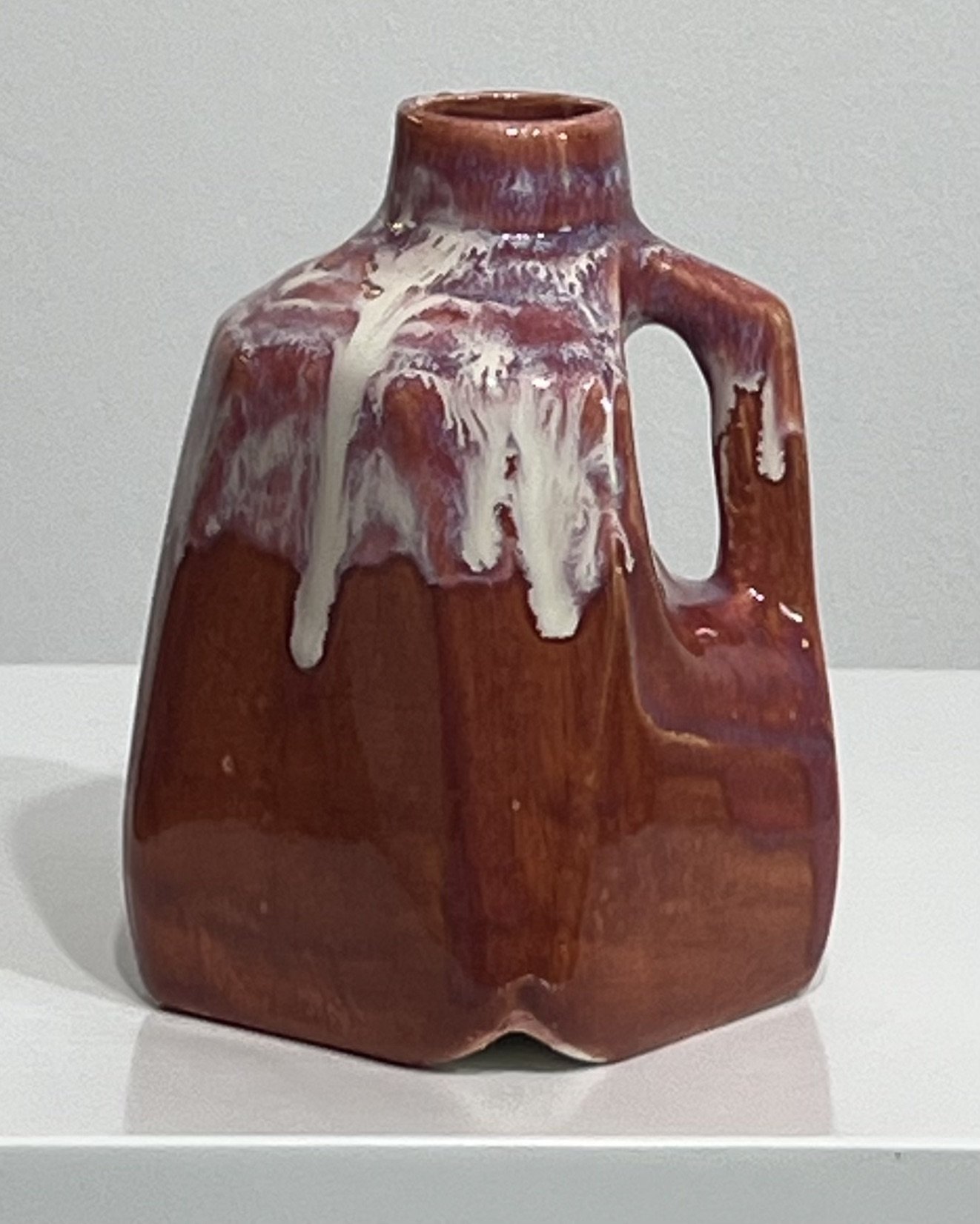 Front view of rust-red porcelain milk jug with flowing ivory and blush glaze